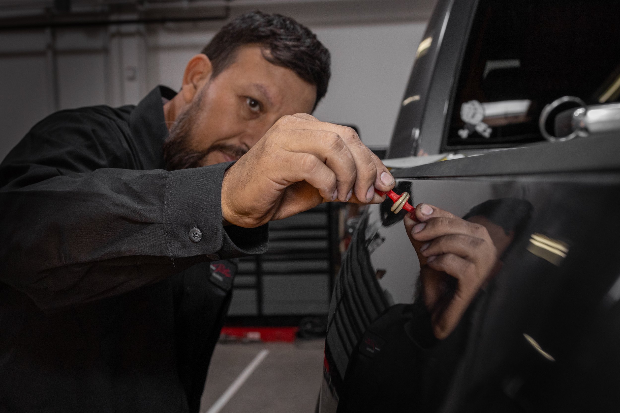 Technician performing paintless dent repair on car door panel in Oxnard auto body shop