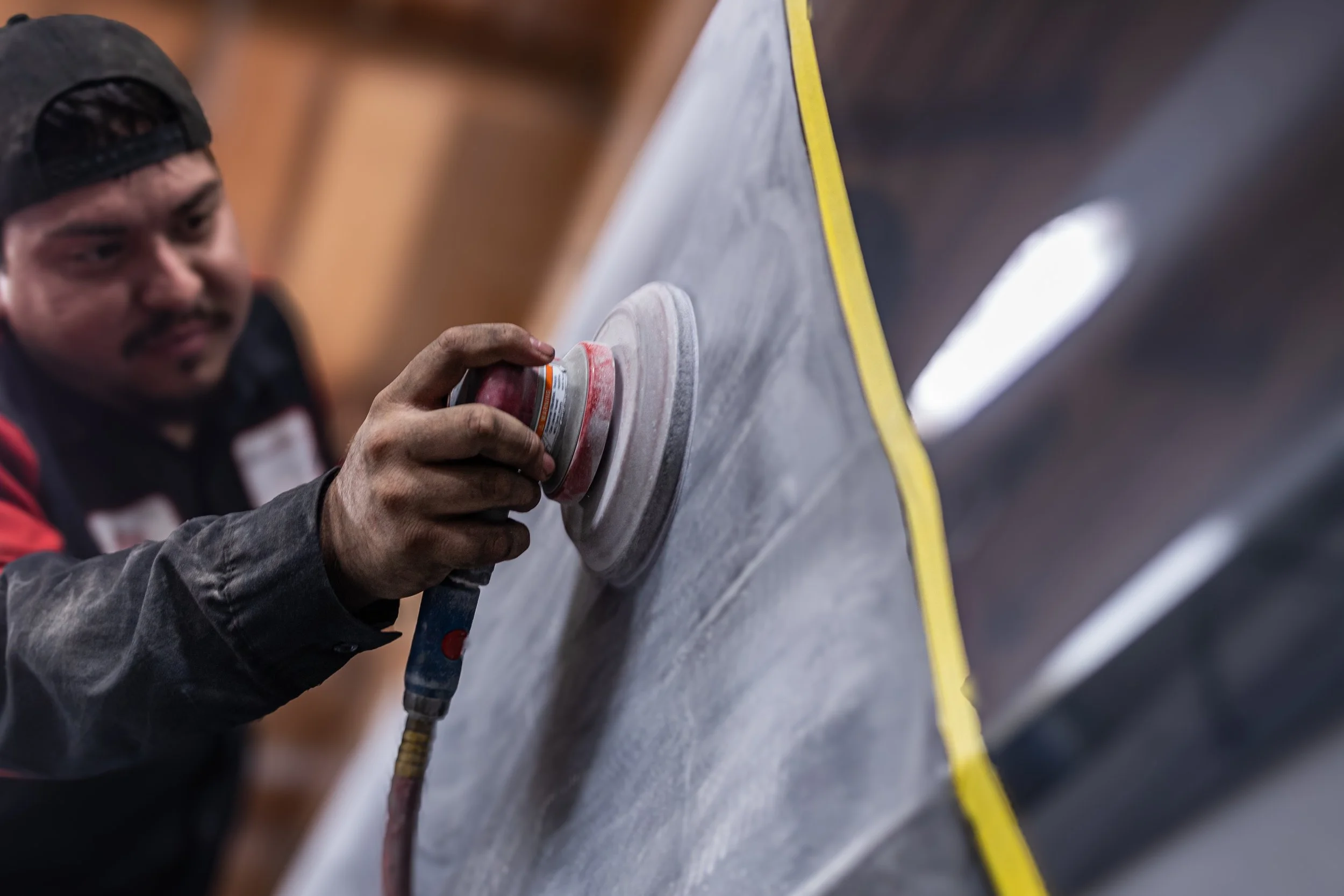 Auto body technician sanding a car panel during paint preparation at a collision repair shop in Oxnard.