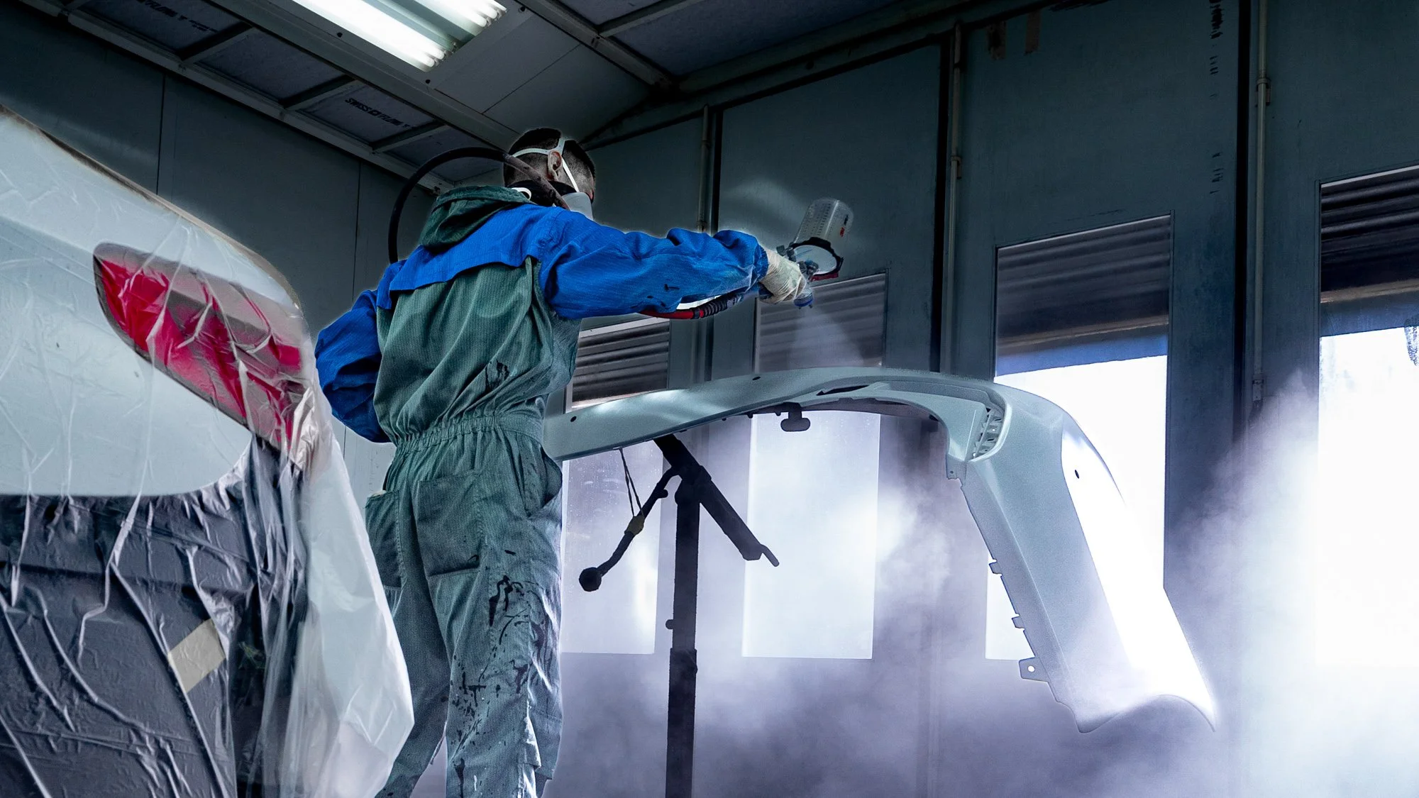 Collision repair painter spraying automotive paint inside a professional paint booth.
