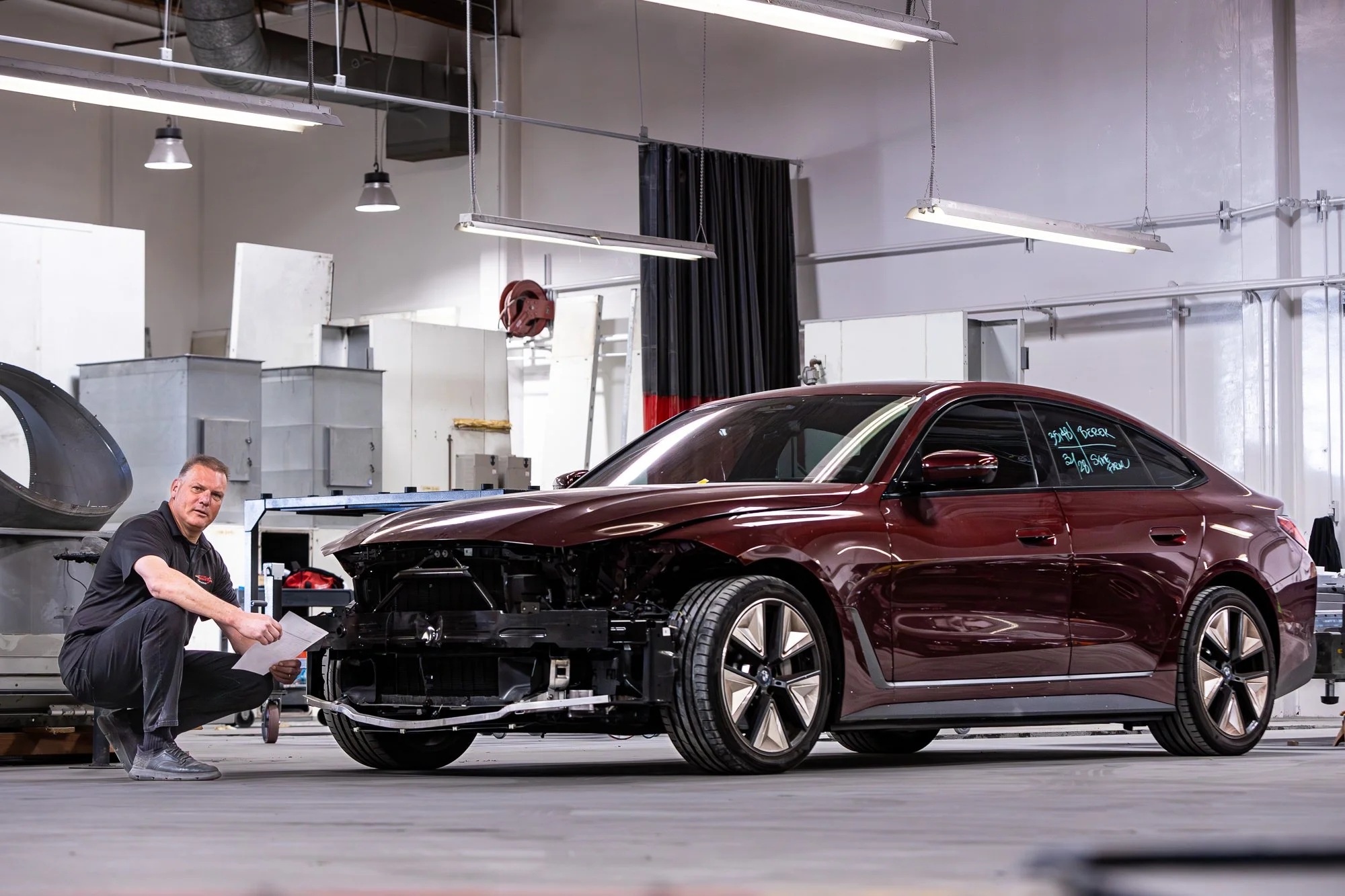 Technician reviewing repair estimate next to damaged vehicle during collision inspection