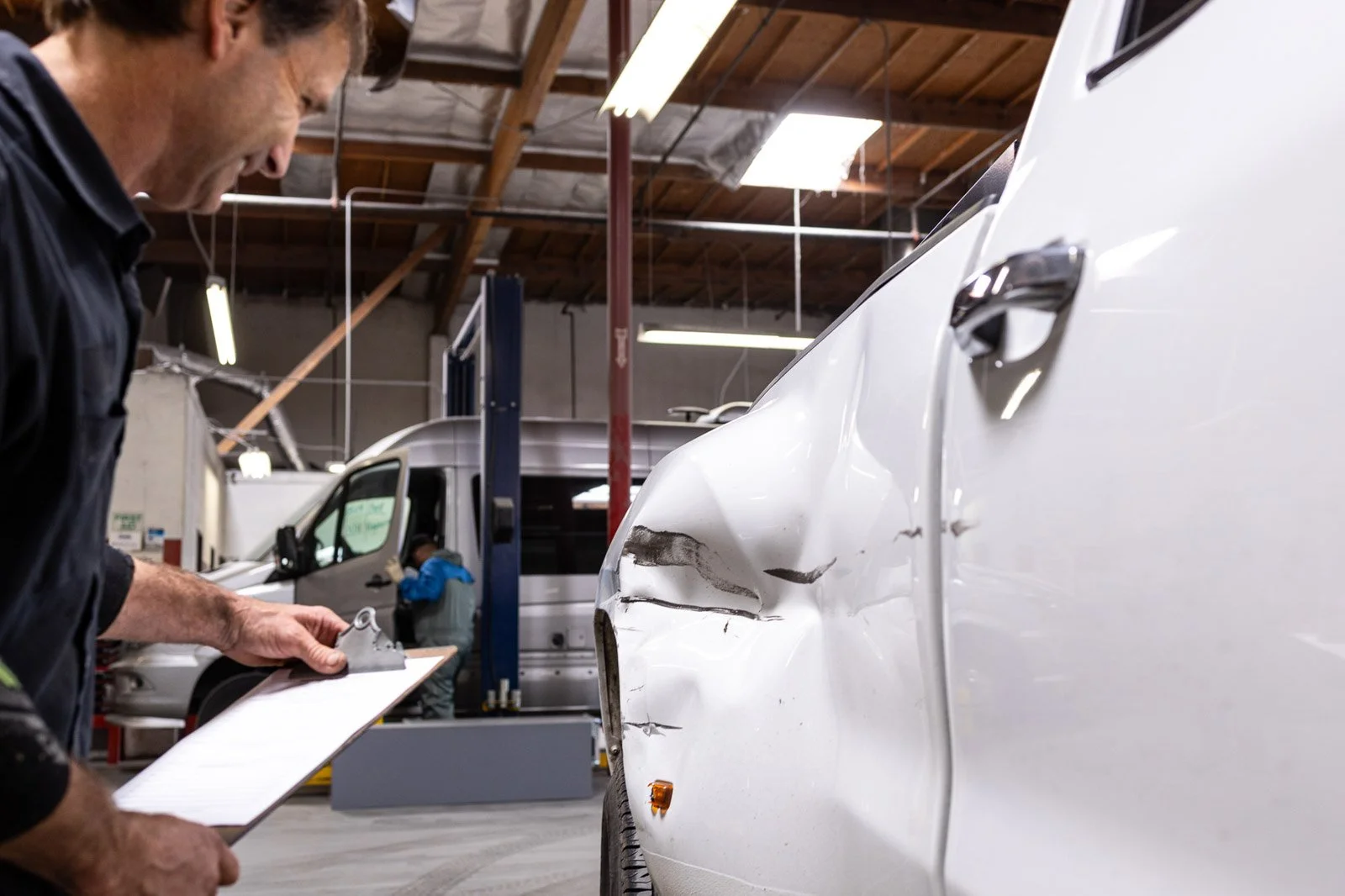 Technician inspecting accident damage on a vehicle in a collision repair facility at Prestige Bodyworks in Oxnard