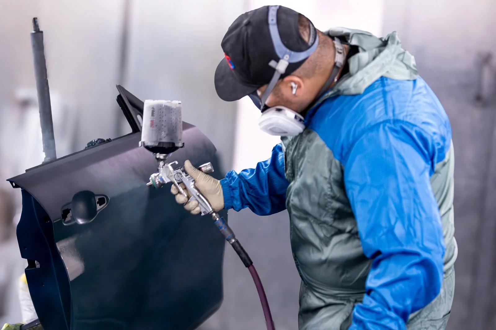 Technician applying paint to car door during collision repair in Oxnard auto body shop