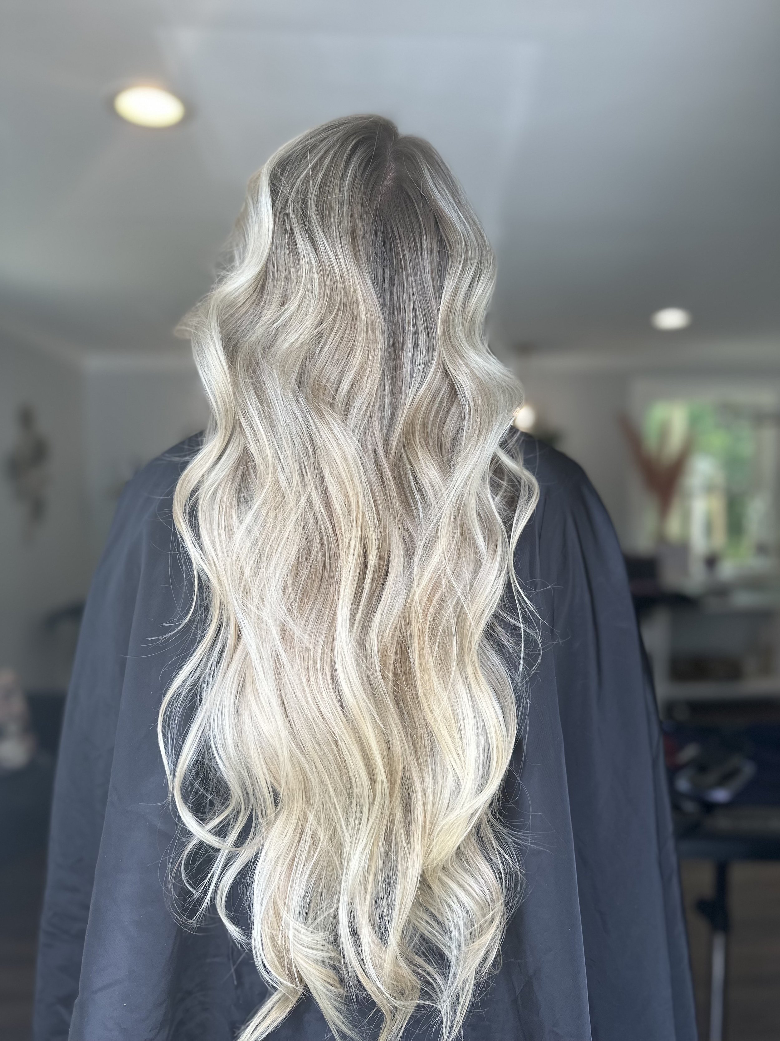 Woman with long, wavy, blonde hair indoors, facing away from the camera.
