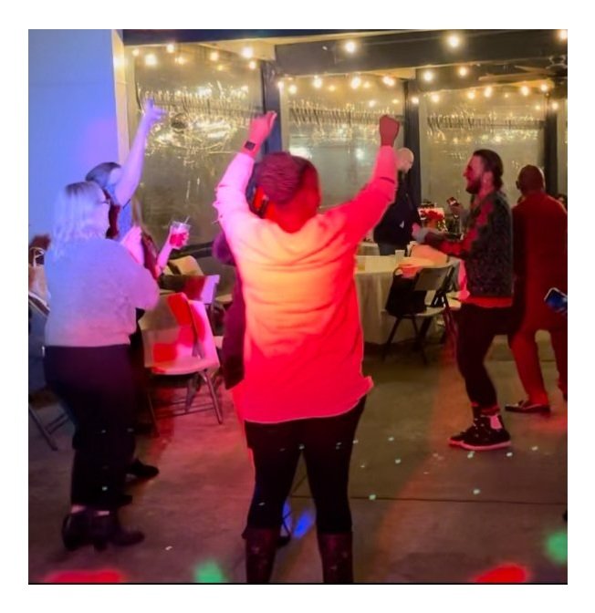 People dancing and enjoying themselves at a party with string lights overhead and a large window in the background.