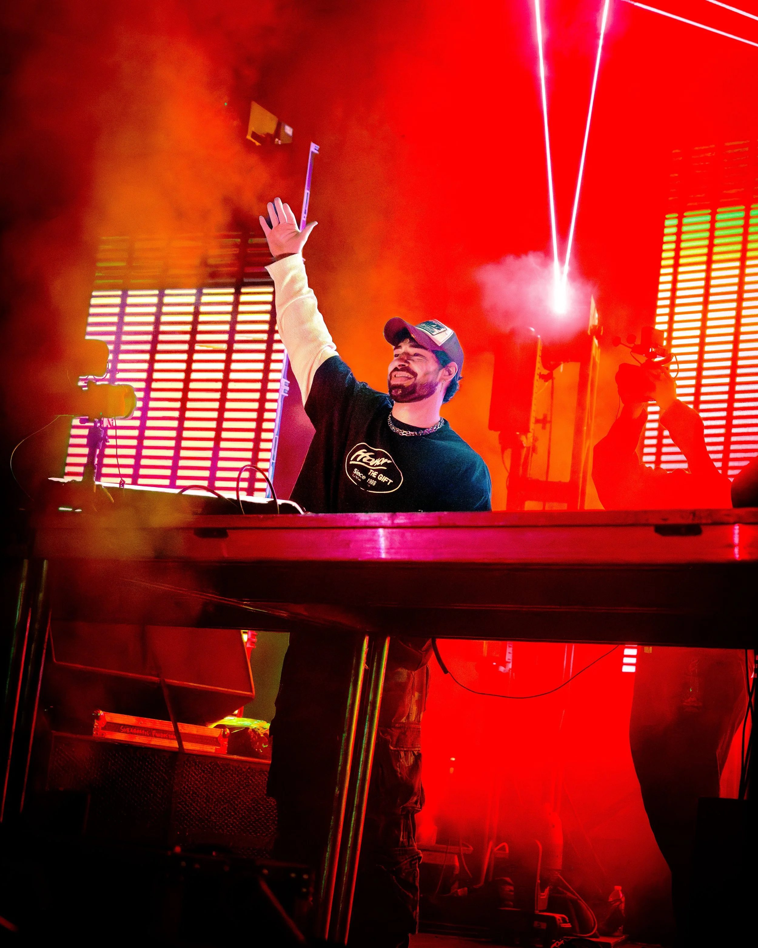 Concert photography of a DJ performing under red stage lights with smoke and lasers.