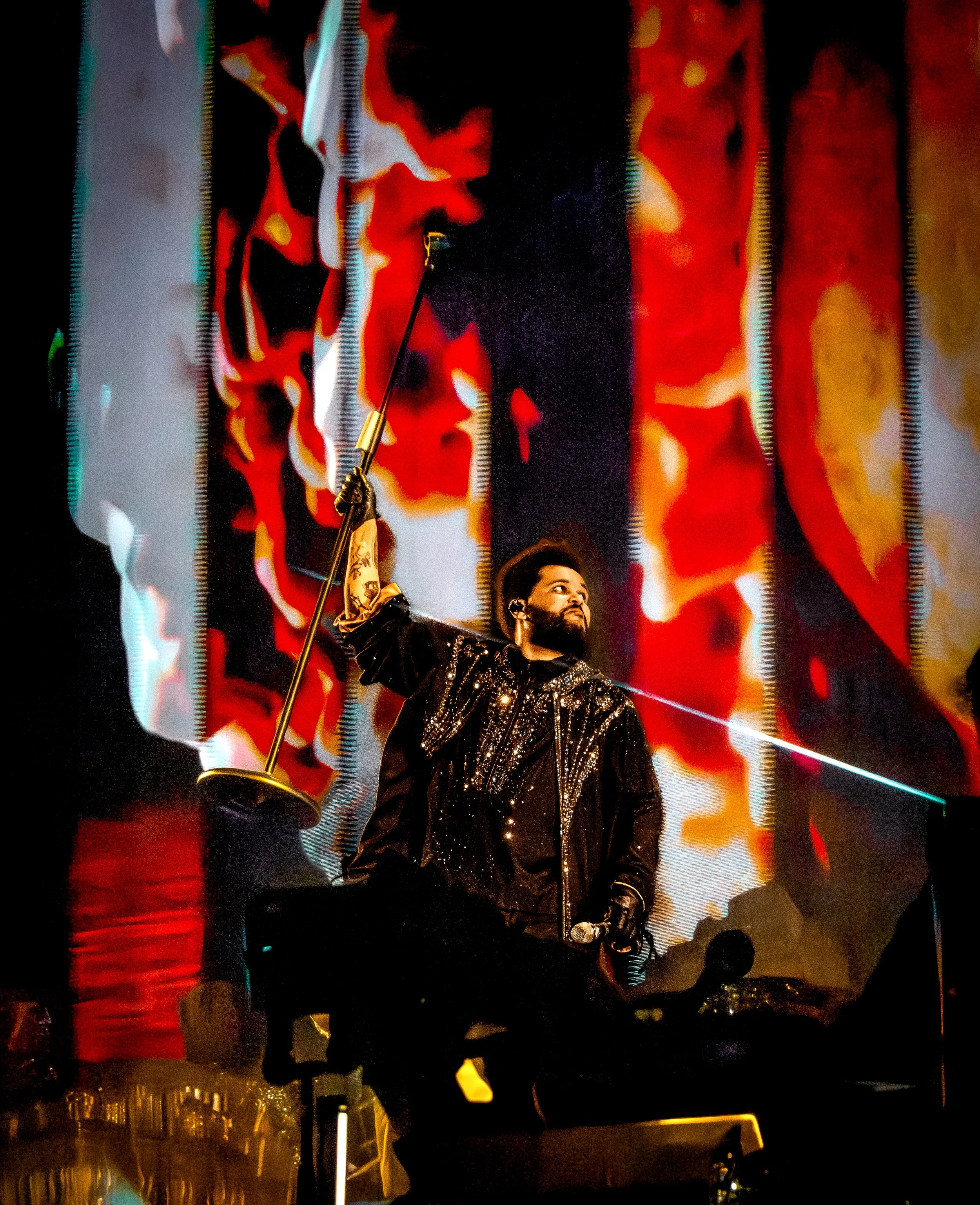 Live concert photography of a singer/performer, The Weeknd, on stage with fiery visuals and dramatic lighting.