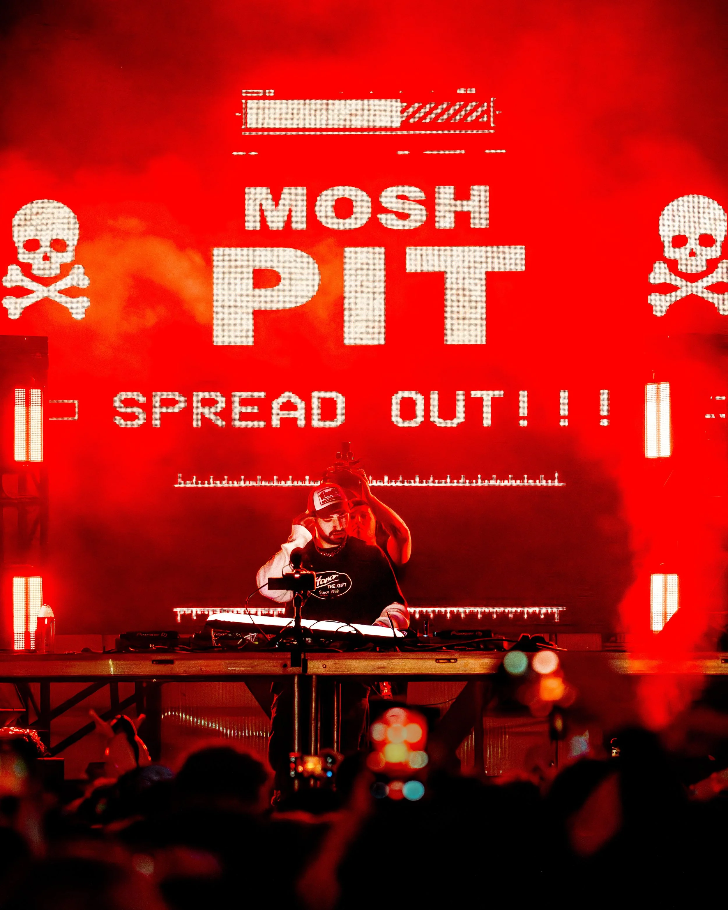 Live music photography of a DJ performing in front of a mosh pit screen during a high-energy set.