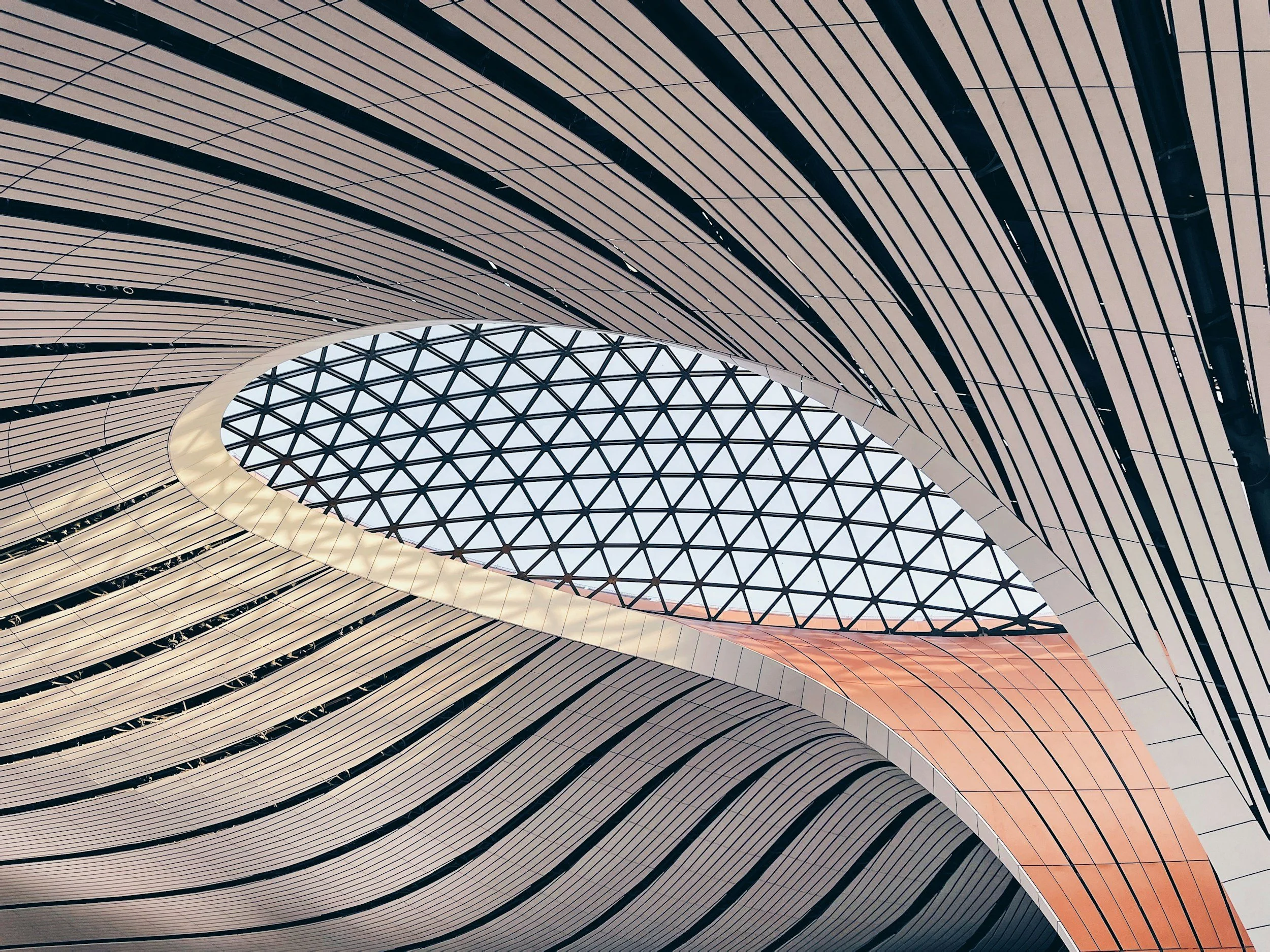 Interior view of a modern building with a curved ceiling and a large glass ceiling in a geometric pattern.