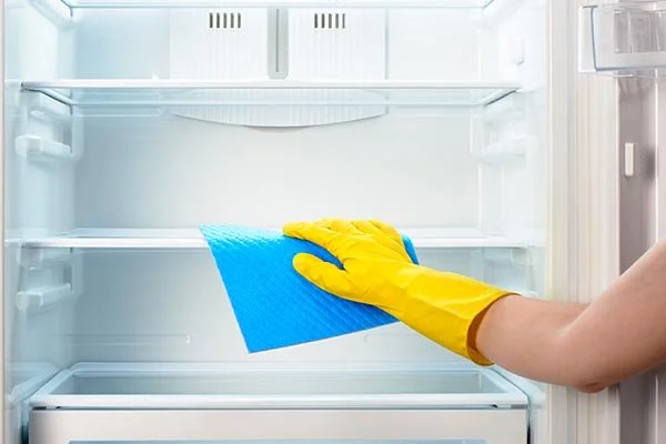 yellow-gloved-hand-wipes-down-empty-fridge-with-rag.jpg