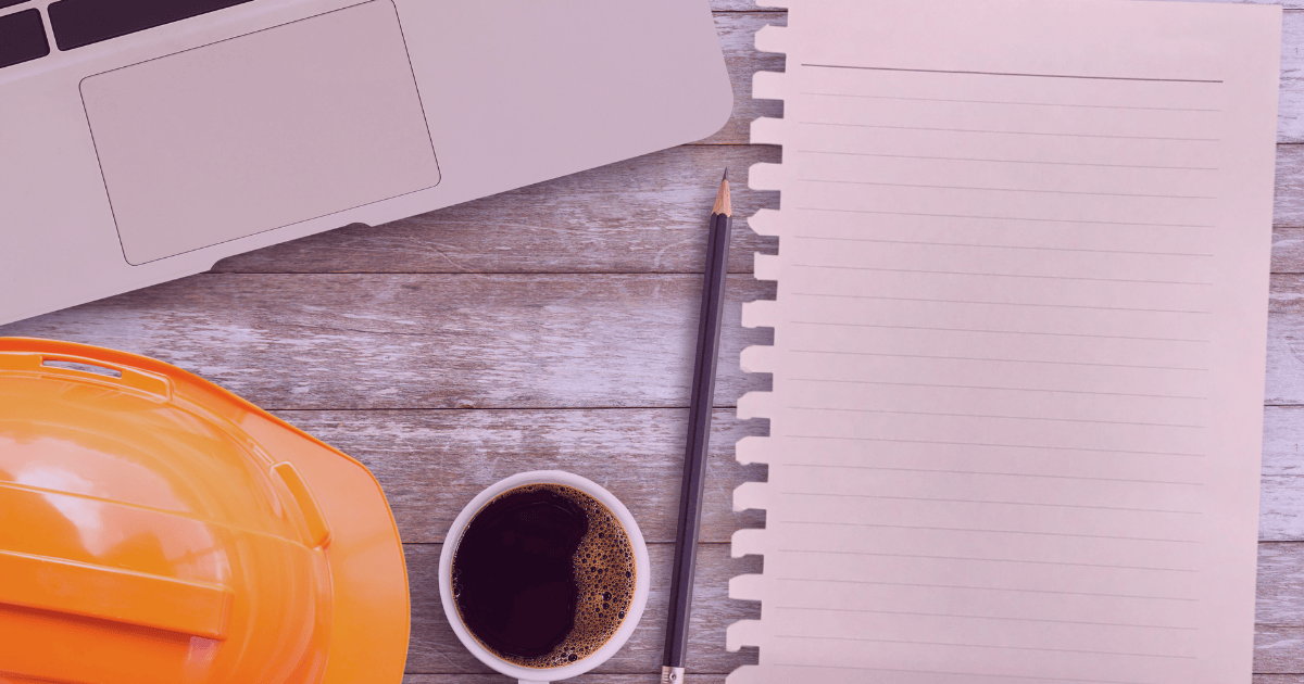A hard hat, laptop, coffee, and notebook on a desk, representing job site planning, organization, and preparing for the next steps.