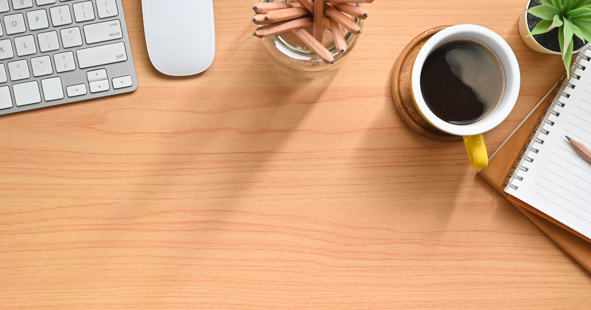 Overhead view of a neat wooden desk with a coffee cup, notebook, and keyboard, representing the administrative side of contracting.