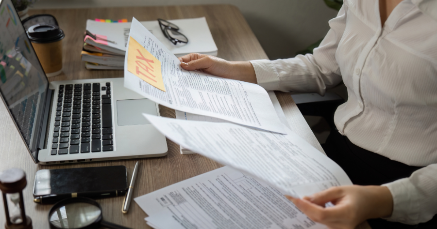 Professional reviewing business documents at a desk with a laptop, illustrating progress through completing capability statements and paperwork.