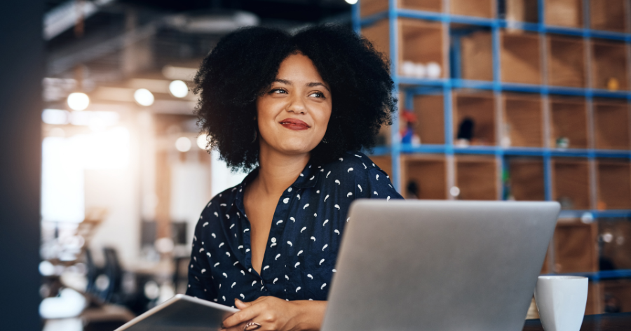Woman-owned small business professional smiling while working at a laptop, representing confidence gained from completing small business tasks.