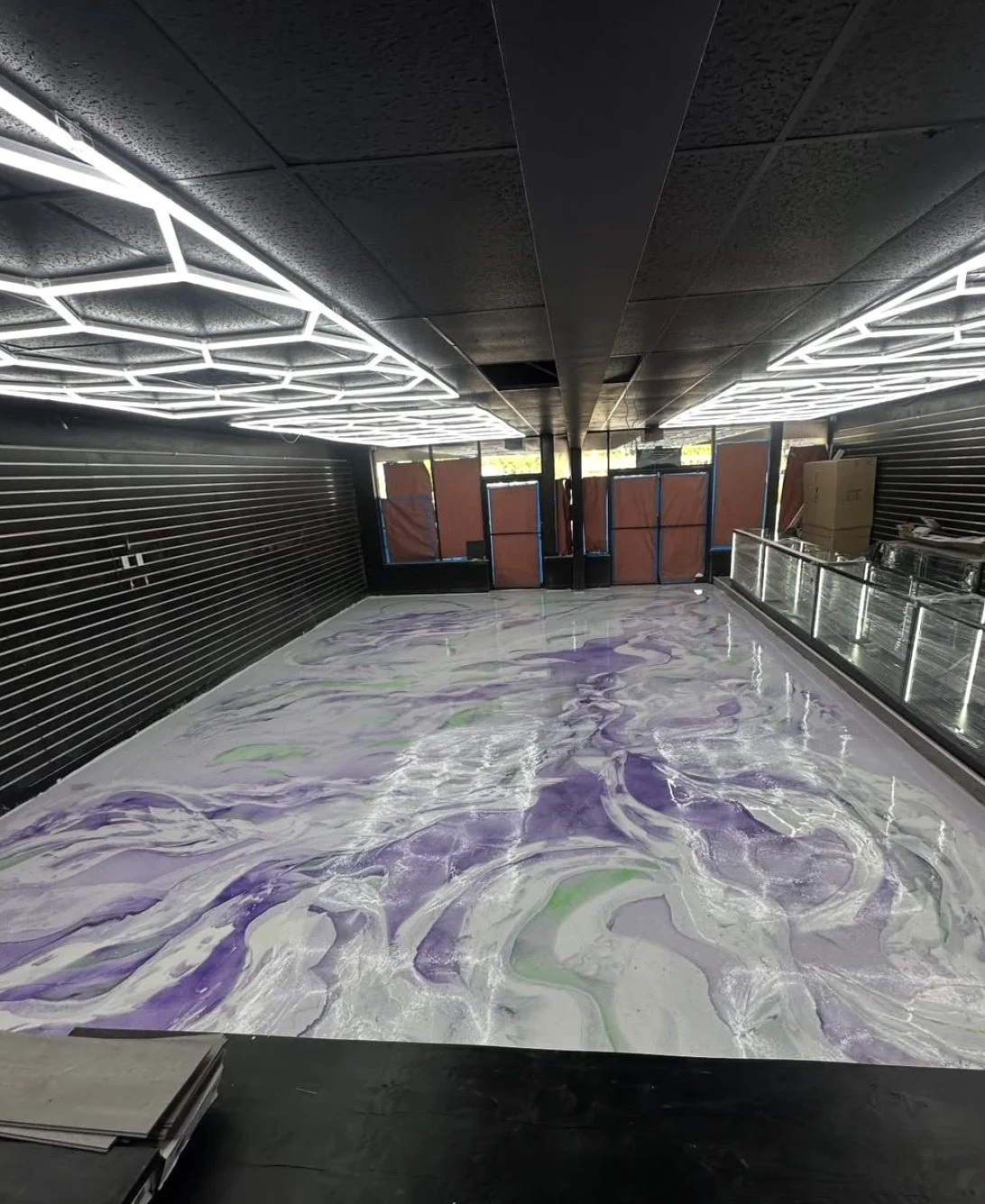 Empty interior space with a swirling purple and white marble floor pattern, black walls with horizontal slats, and modern geometric LED ceiling lights, possibly under renovation or construction.