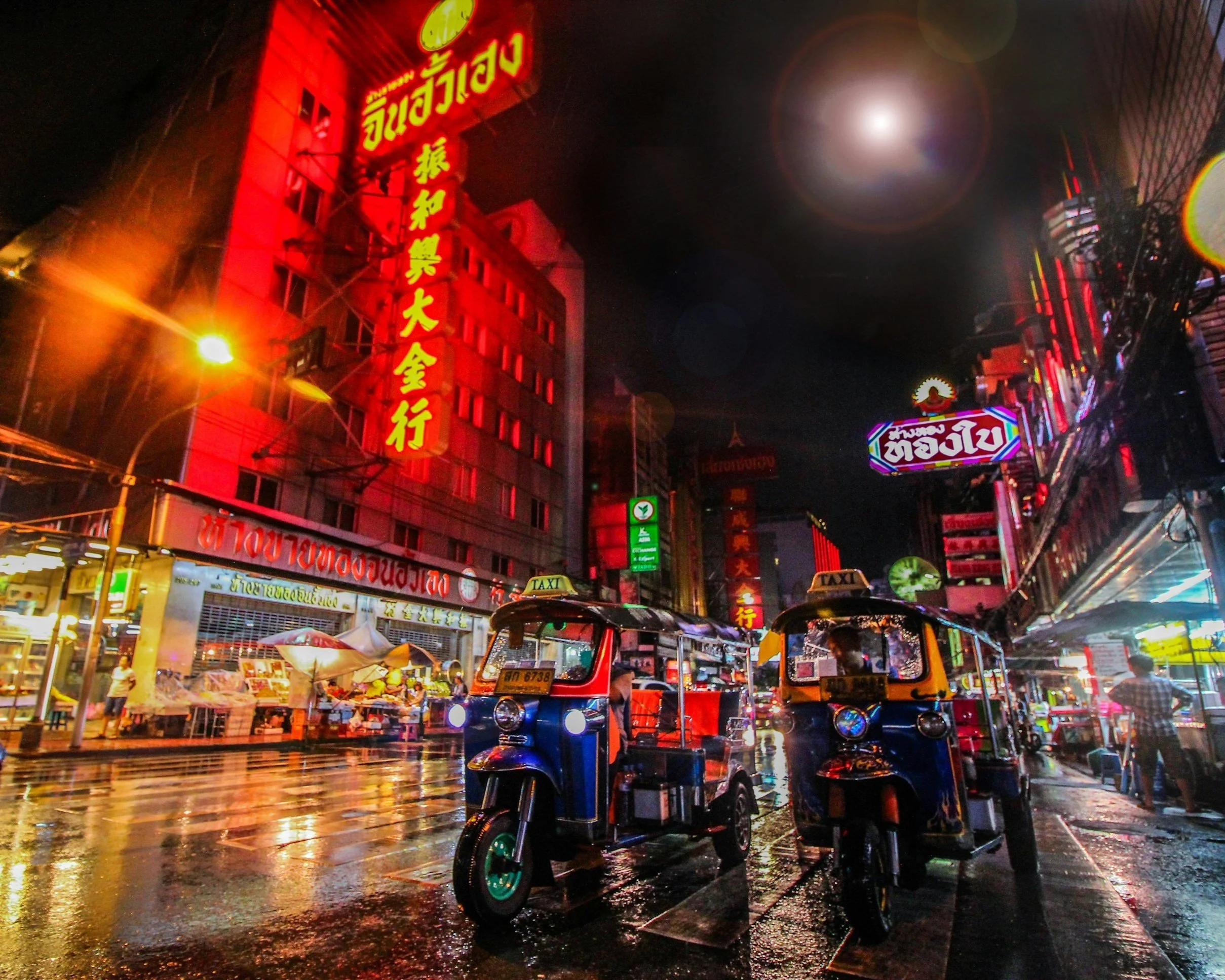 Night scene of a busy street in Bangkok's Chinatown with neon signs and tuk-tuks.