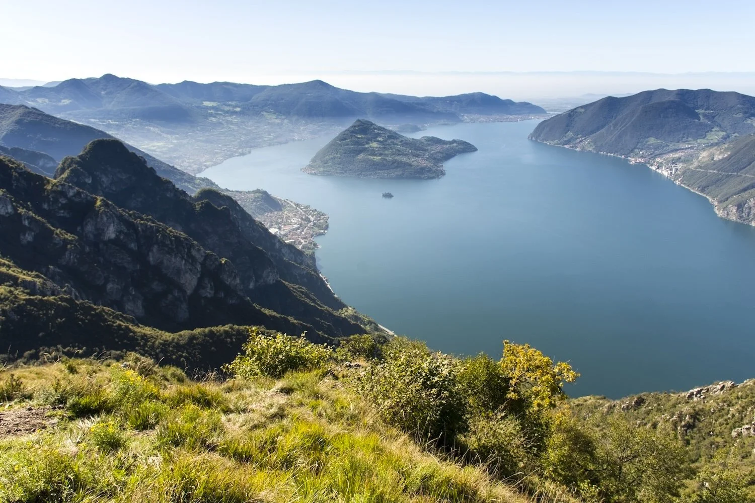 Aerial view of a large lake surrounded by green mountains and hills with a small island in the middle.