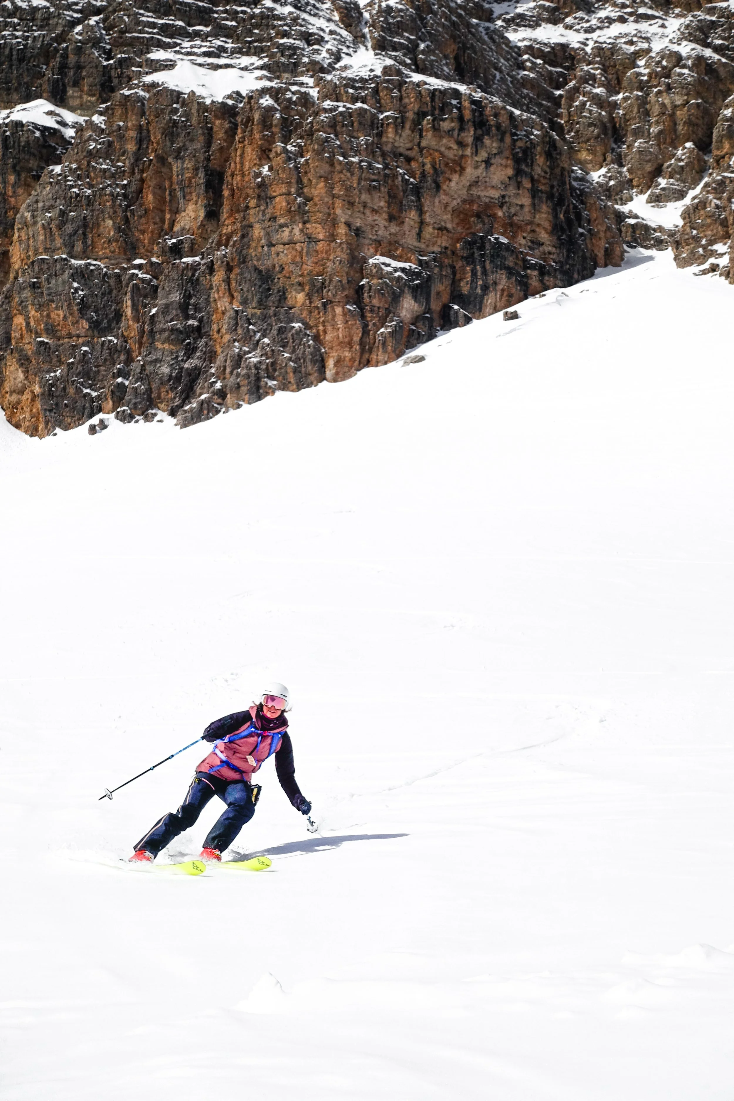 A woman skiing on snow with a rocky mountain in the background.