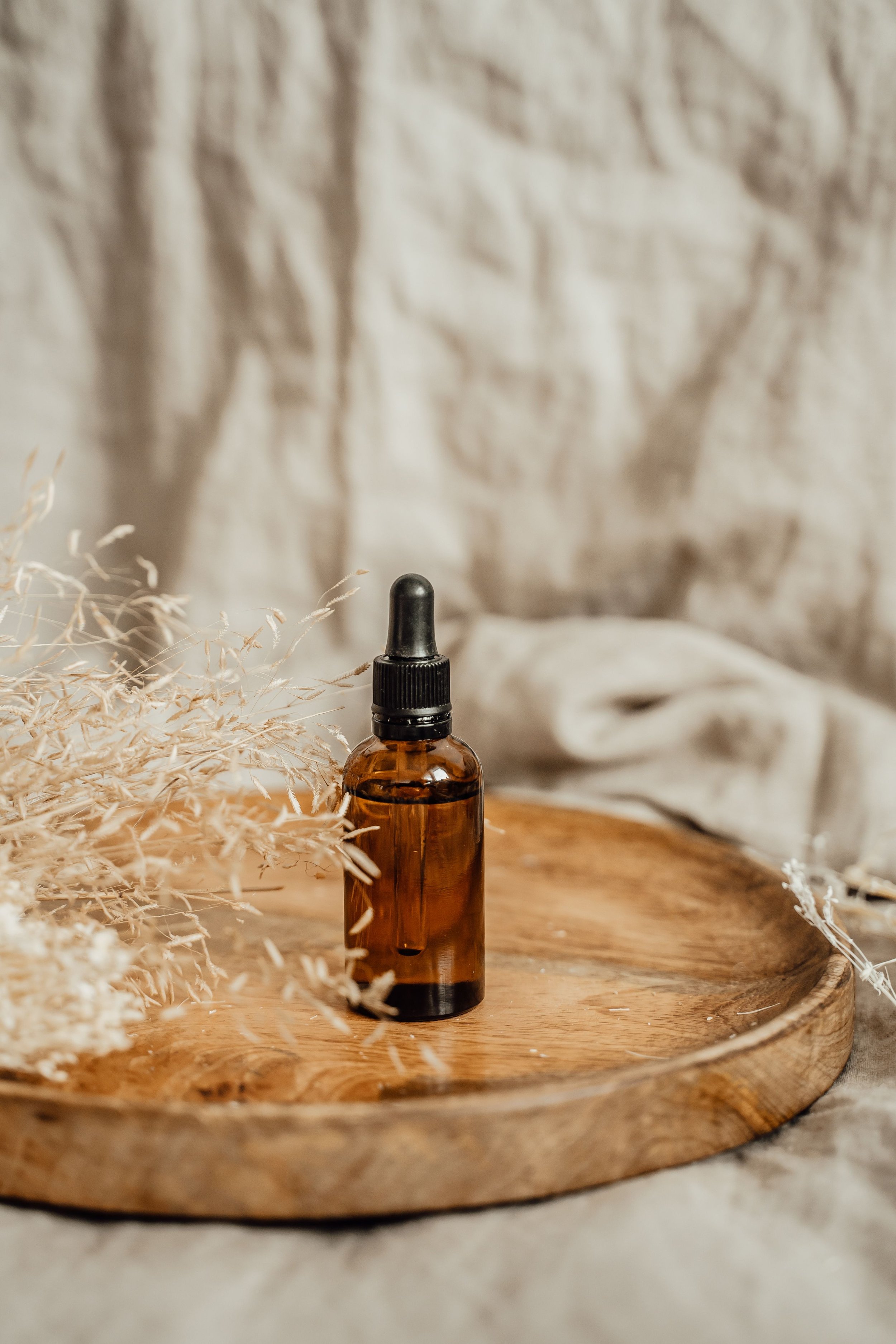 Une bouteille en verre ambré avec un compte-gouttes noir, posée sur une surface en bois, entourée de branches séchées, avec un fond en tissu beige clair.