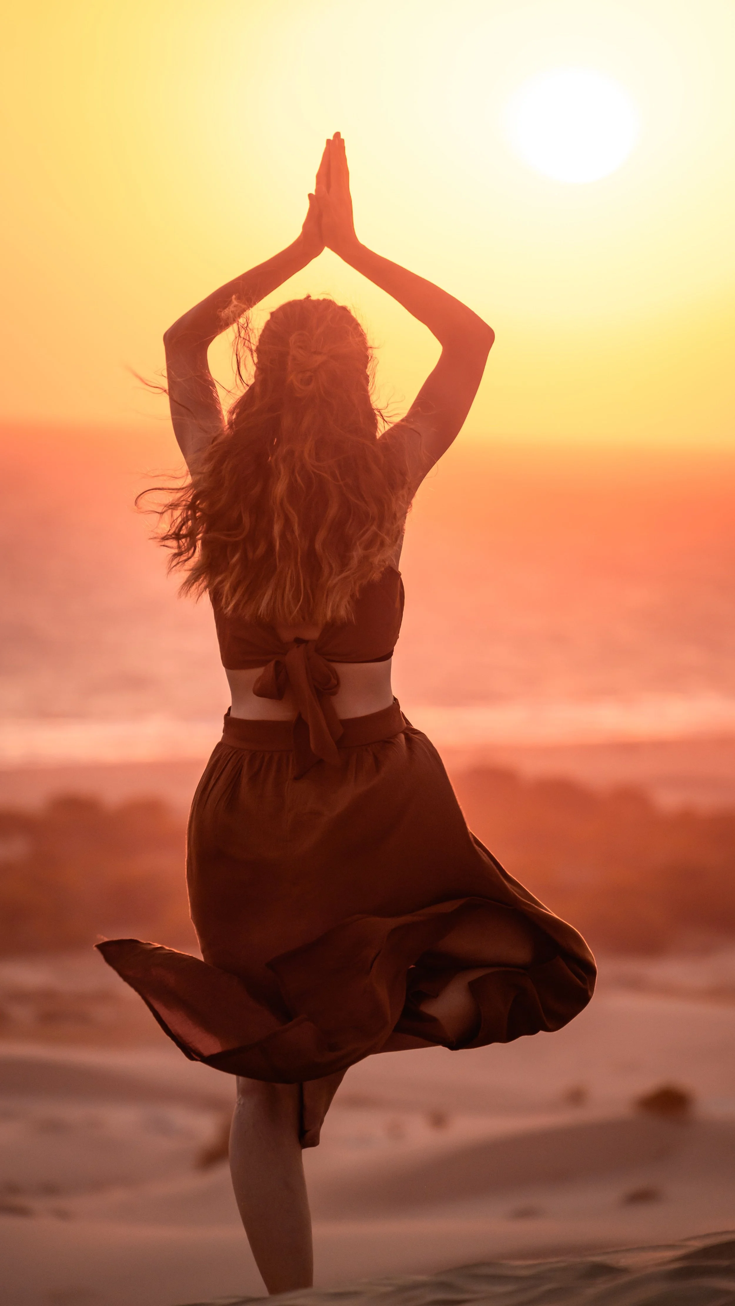 Une femme en position de yoga en méditation au coucher du soleil sur la plage.