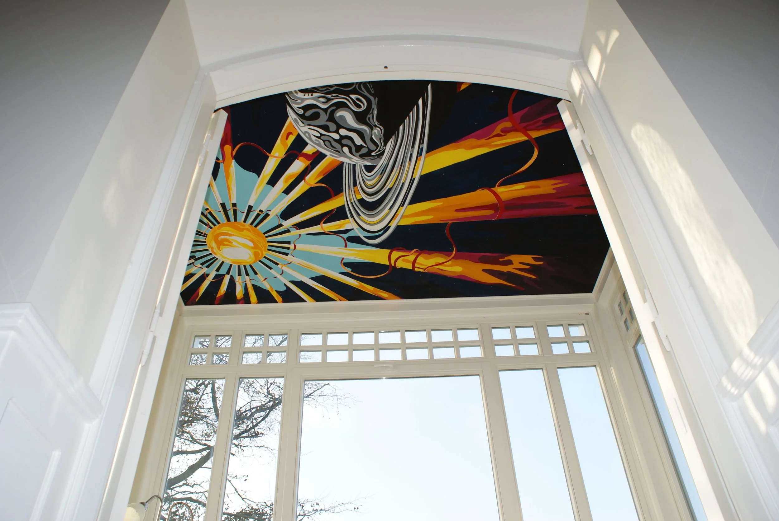 Interior view of a ceiling mural featuring a cosmic scene with abstract planets, stars, and bright colorful streaks of light, viewed from a room with large windows and white trim.