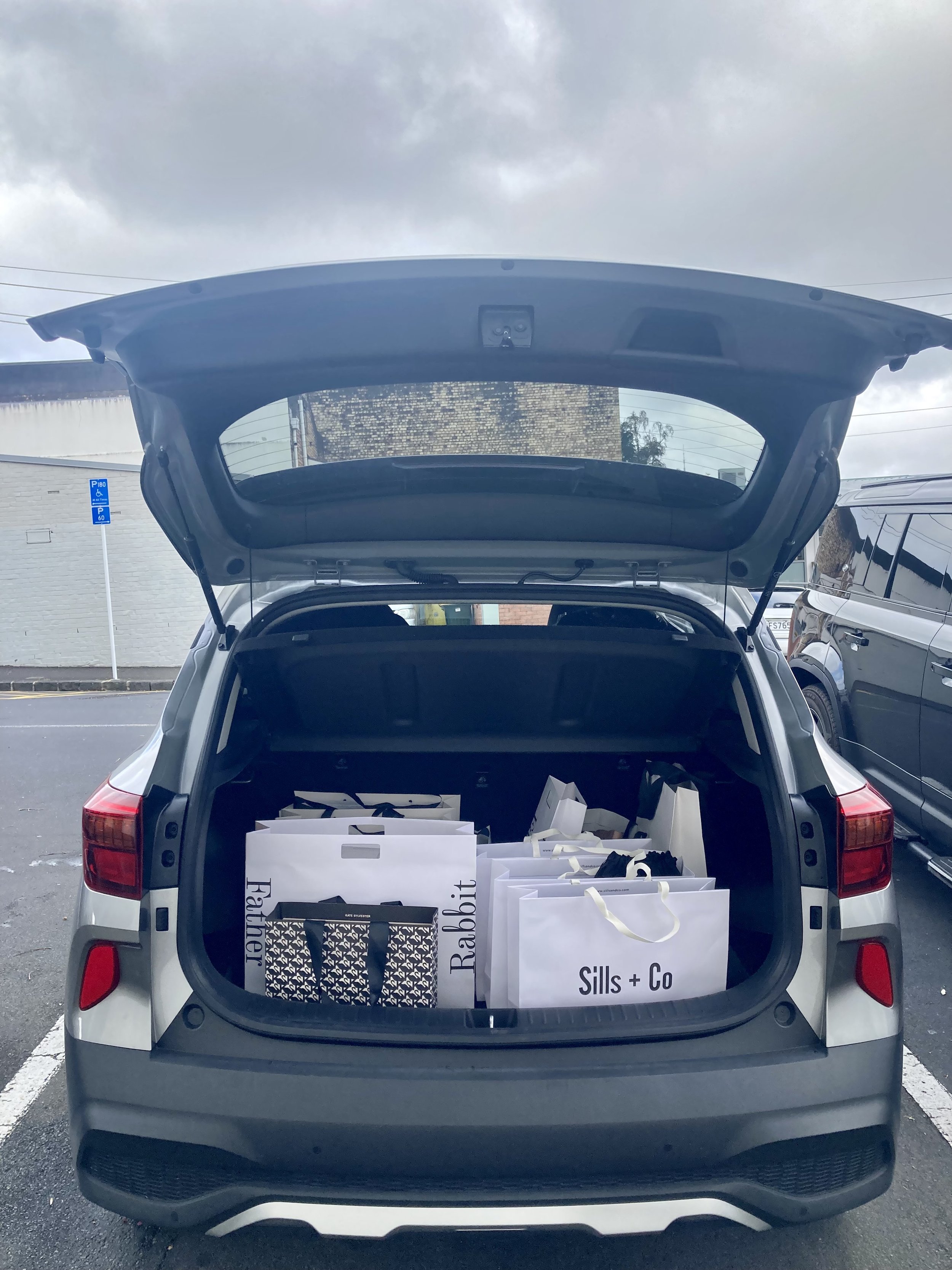 Car trunk filled with shopping bags, The Bespoke Dresser collecting garments for a concierge shop.