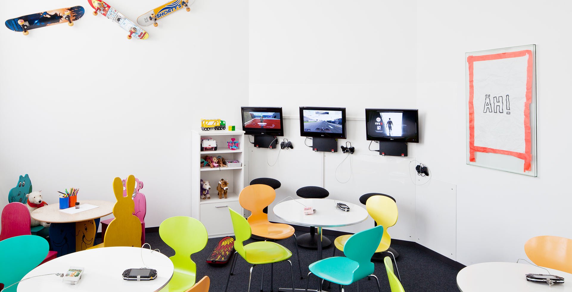 Spielcafé mit bunten Stühlen, Spielzeug, TV-Spielen und Wanddekoration im Kinderzimmer.