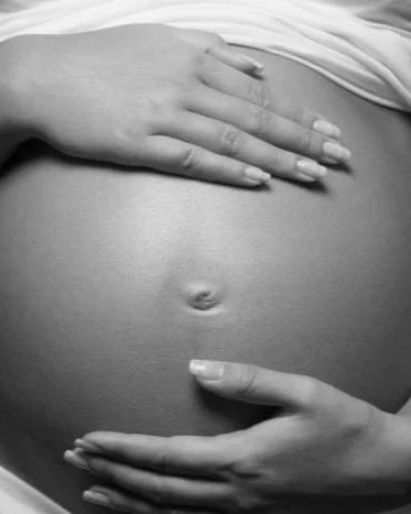 Close-up of a pregnant woman's belly with hands gently resting on it.