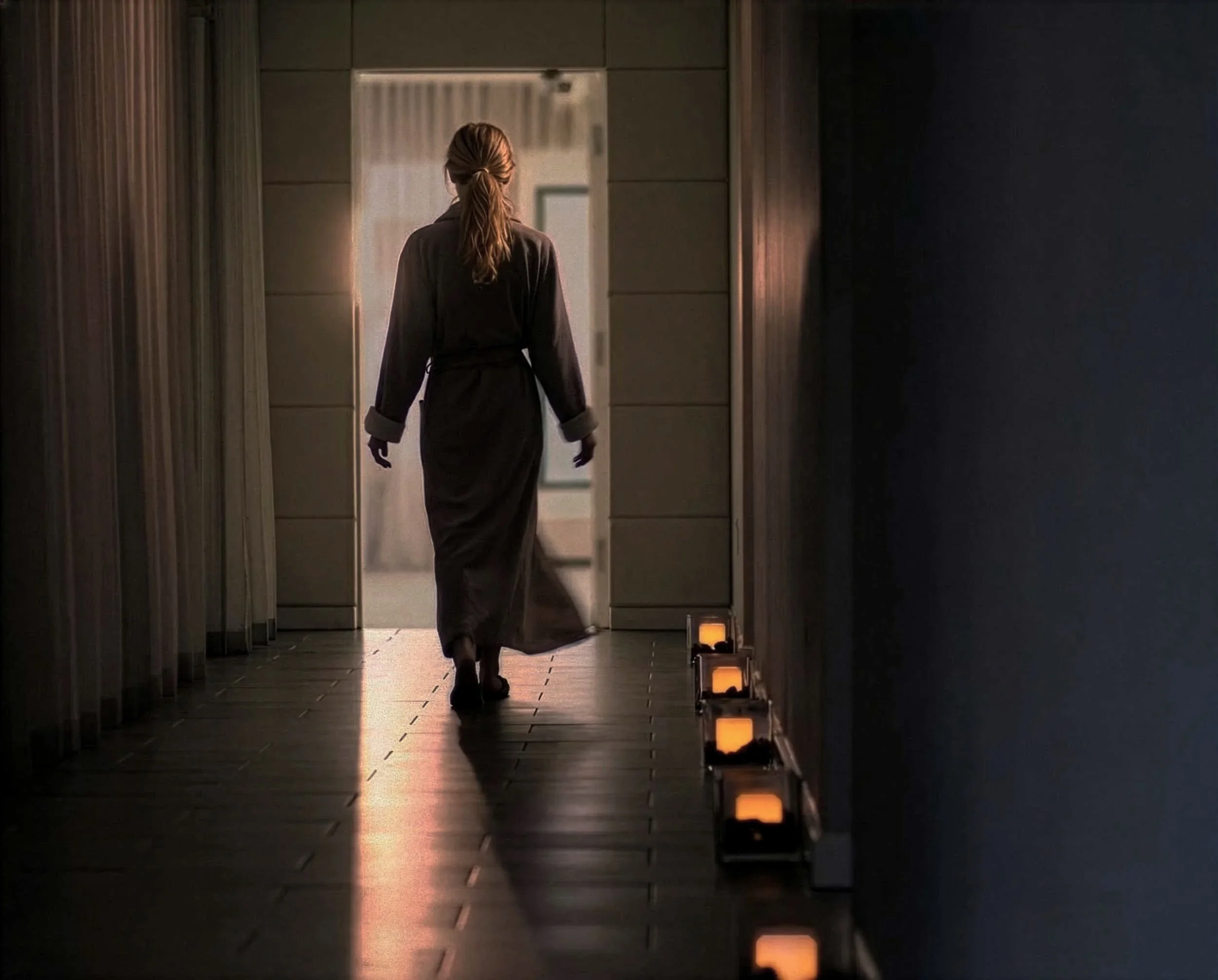 A woman in dark clothing walking through a dimly lit corridor with small lights on the floor.