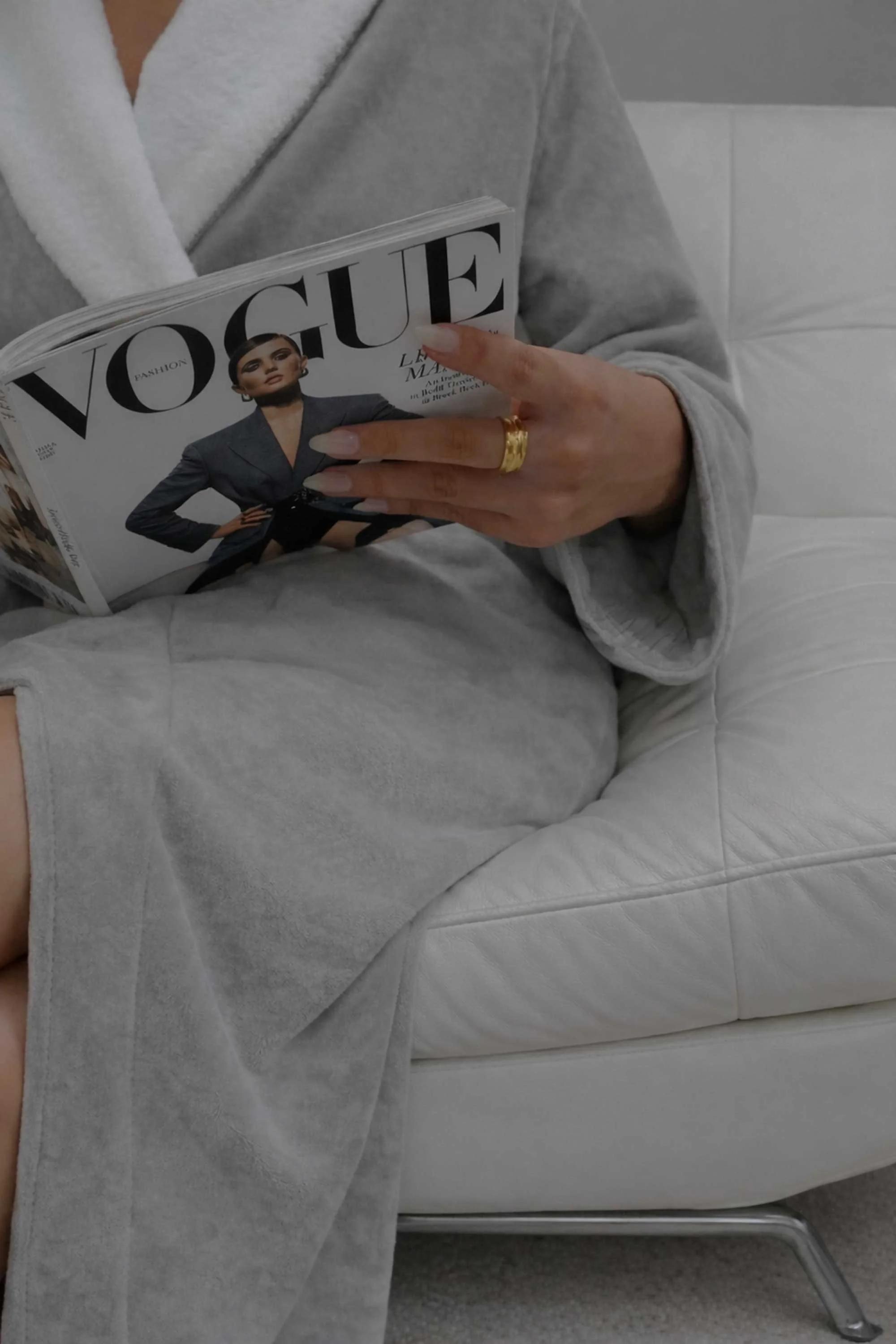 A guest wearing a plush grey robe and gold rings relaxes in the Tranquility Lounge while reading a magazine.