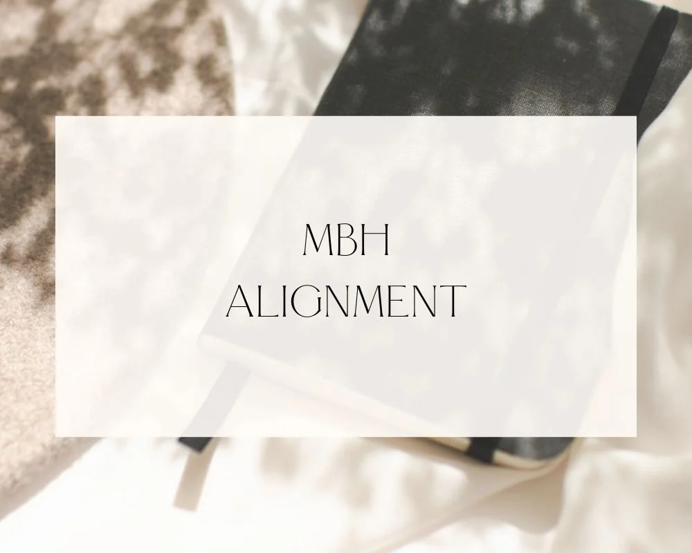 A notebook with a black cover and a white page overlay with text. The text reads "MBH ALIGNMENT."
