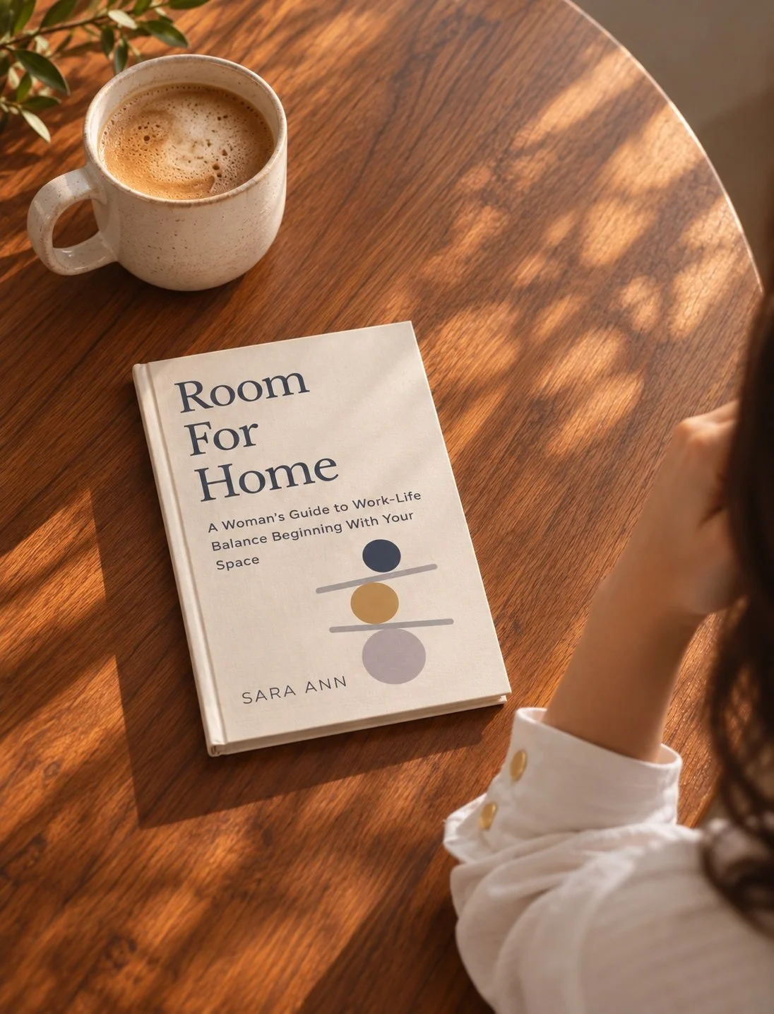 Book titled Room For Home: A Woman's Guide to Work-Life Balance Beginning With Your Space sits on a wooden desk next to woman and cup of coffee.