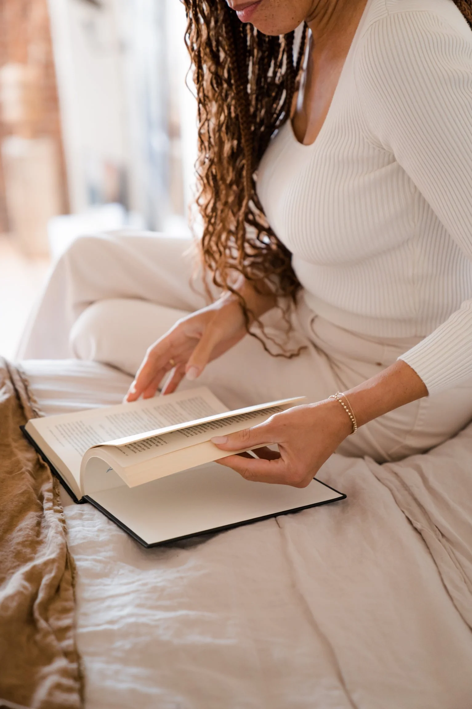 Brown woman sitting on bed flipping through pages of a book