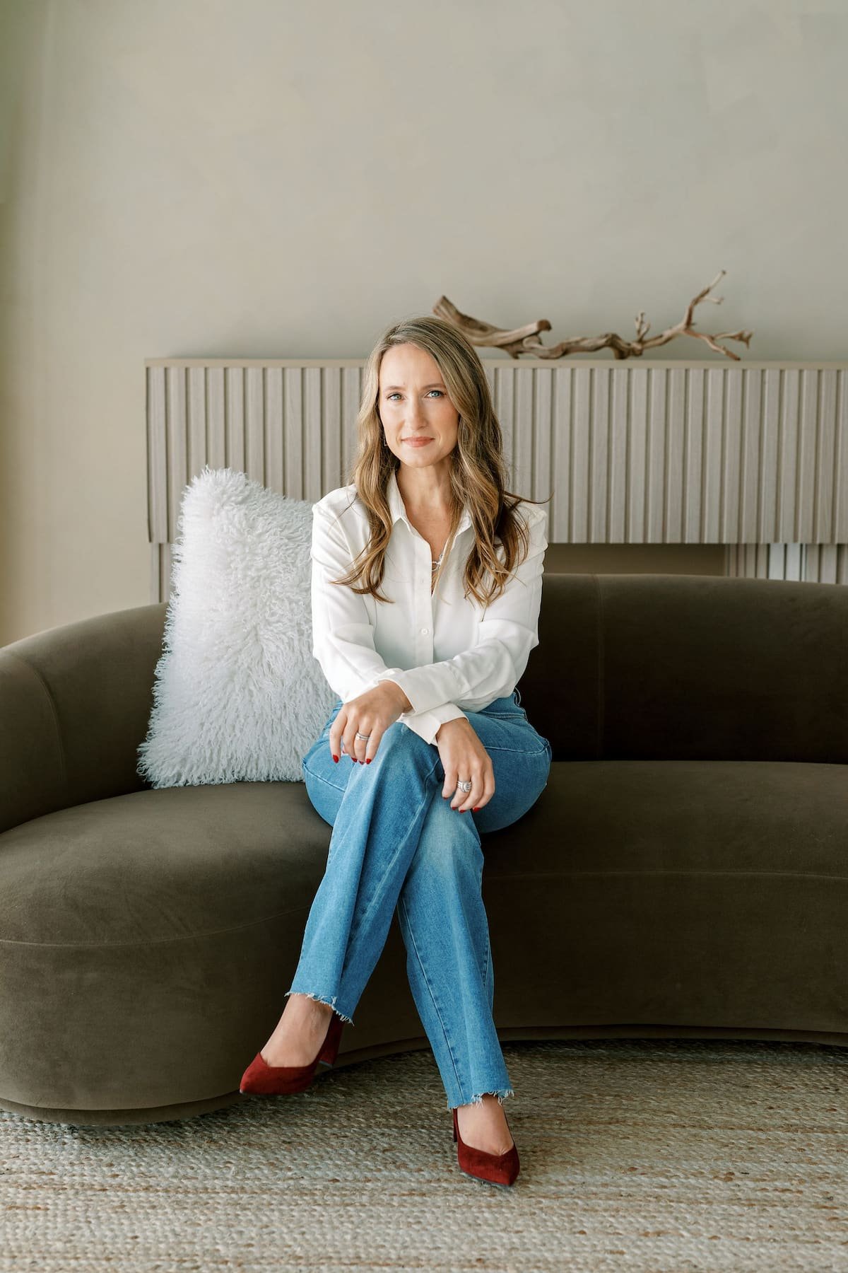 Sara Ann Founder of Jade Scott Design and host of the Mind Body Home podcast sitting on olive green sofa against neutral background