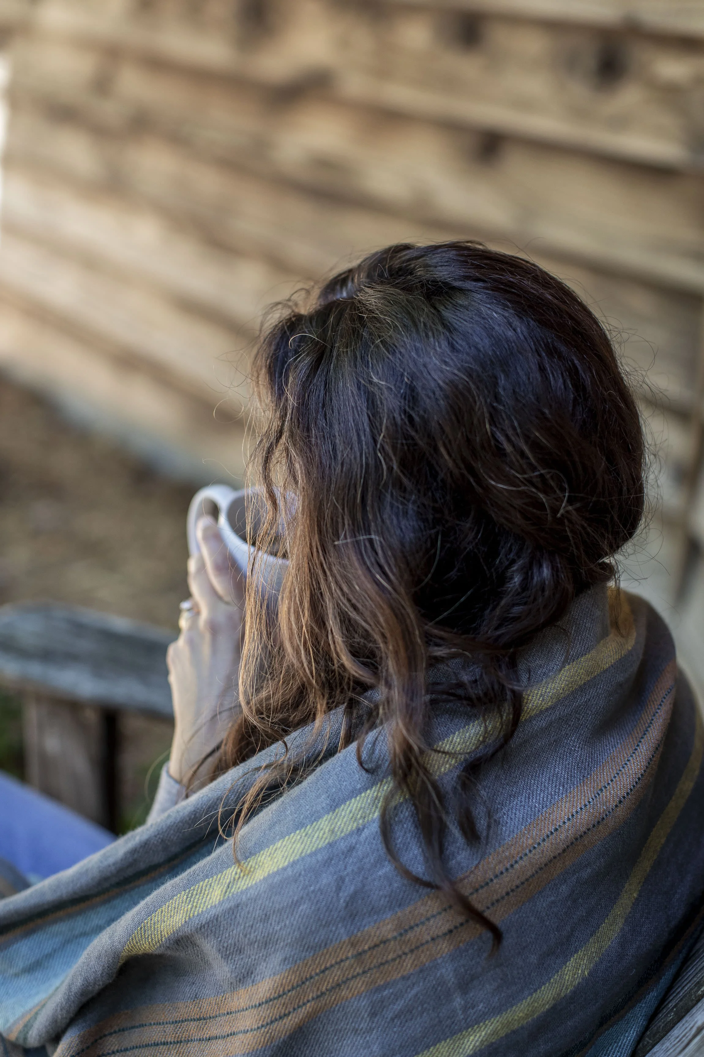 Middle aged woman enjoying a cup of coffee on the porch wrapped in a flannel blanket