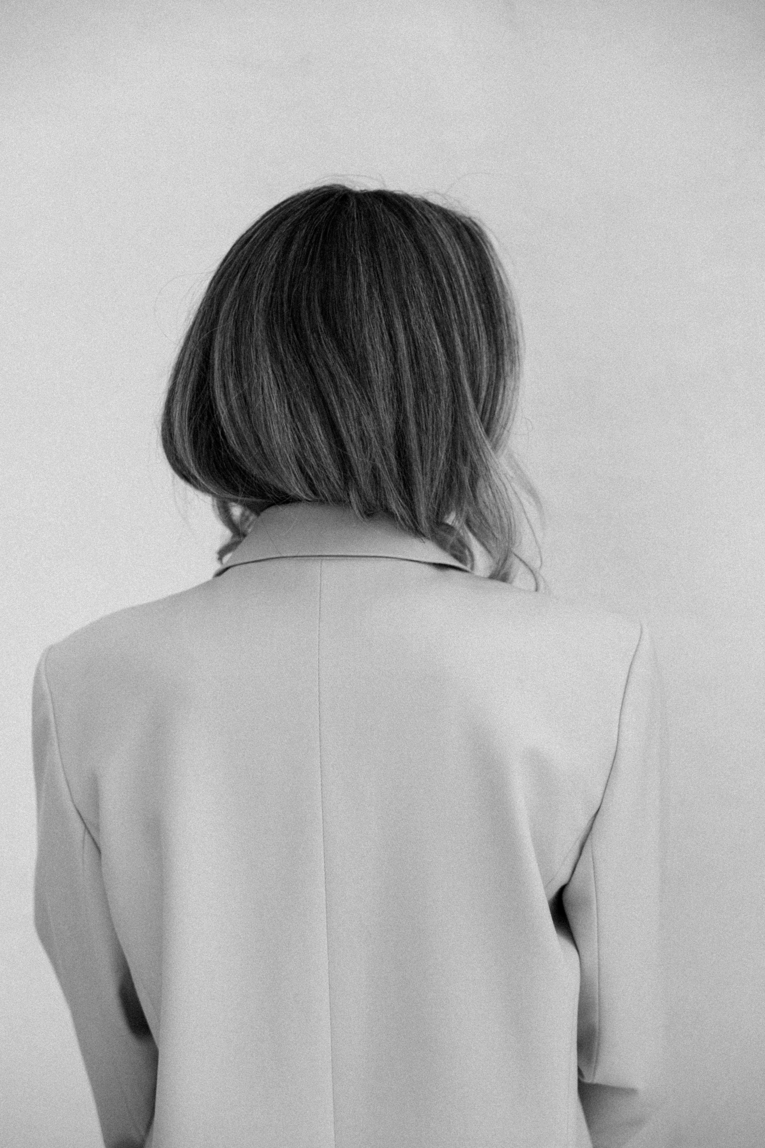 Black and white photo of a woman with short, wavy hair turned away from the camera, wearing a blazer.