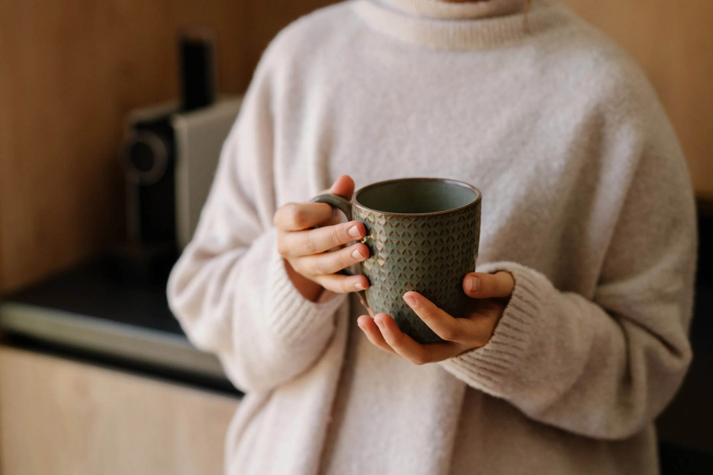 Person wearing a cream-colored sweater holding a textured ceramic mug.