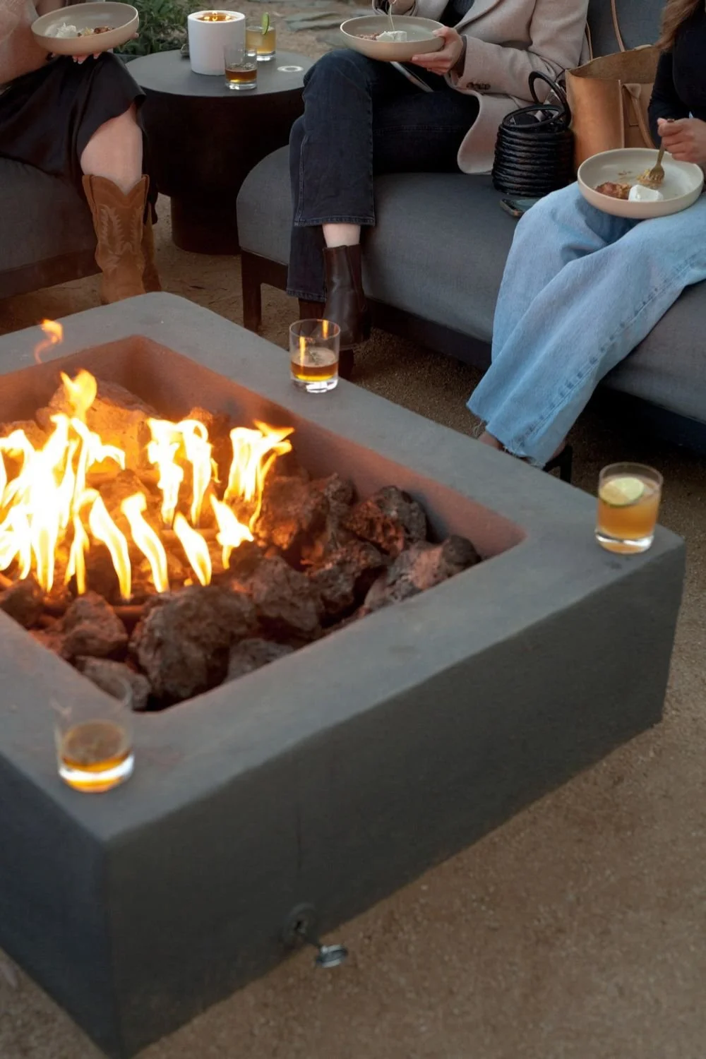Women gathered around a fire pit enjoying food and connection on a cool evening.