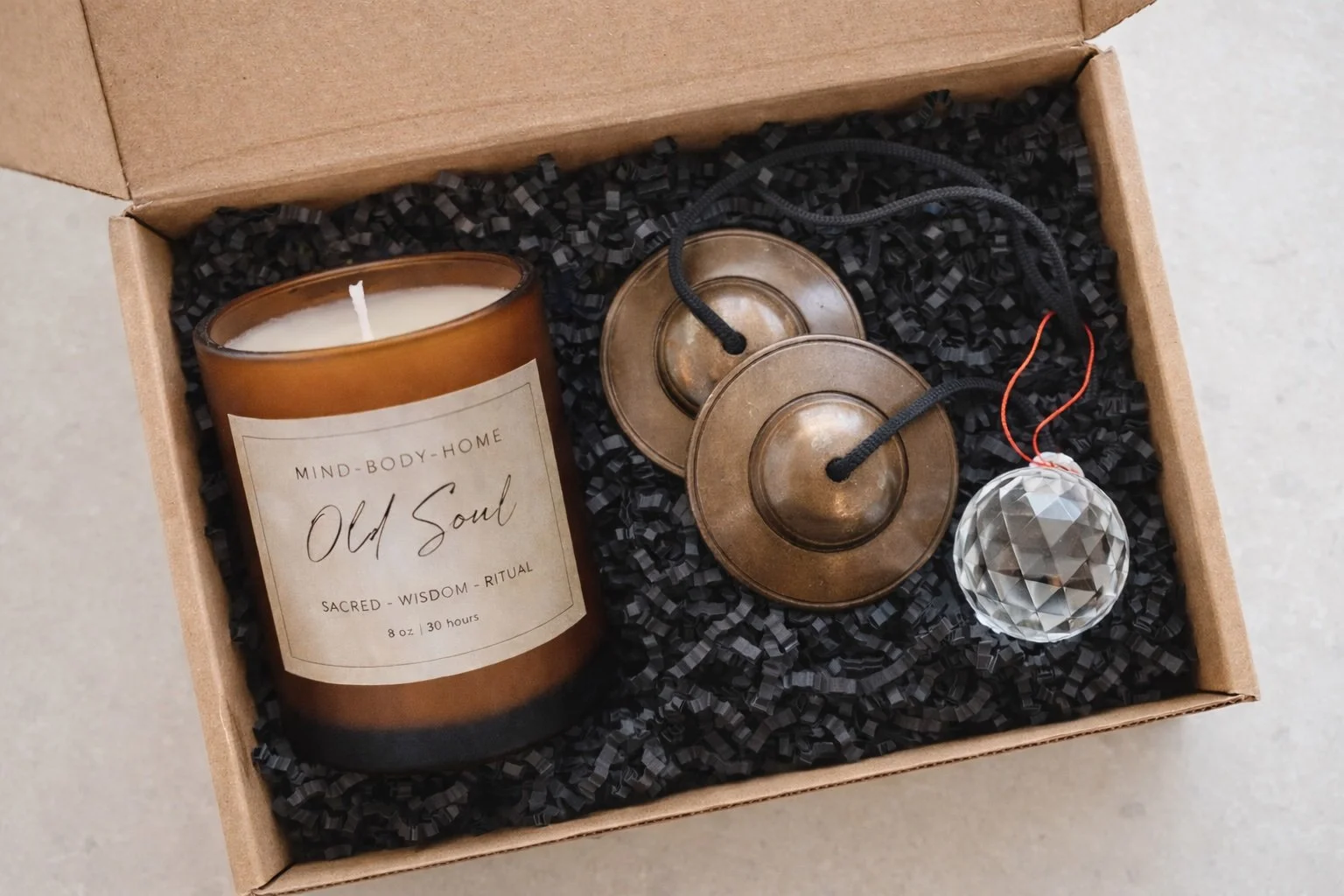 Sacred space clearing kit that includes Old Soul candle, tingsha bells, and faceted crystal ball. This kit is pictured in a Kraft box with black paper shred.