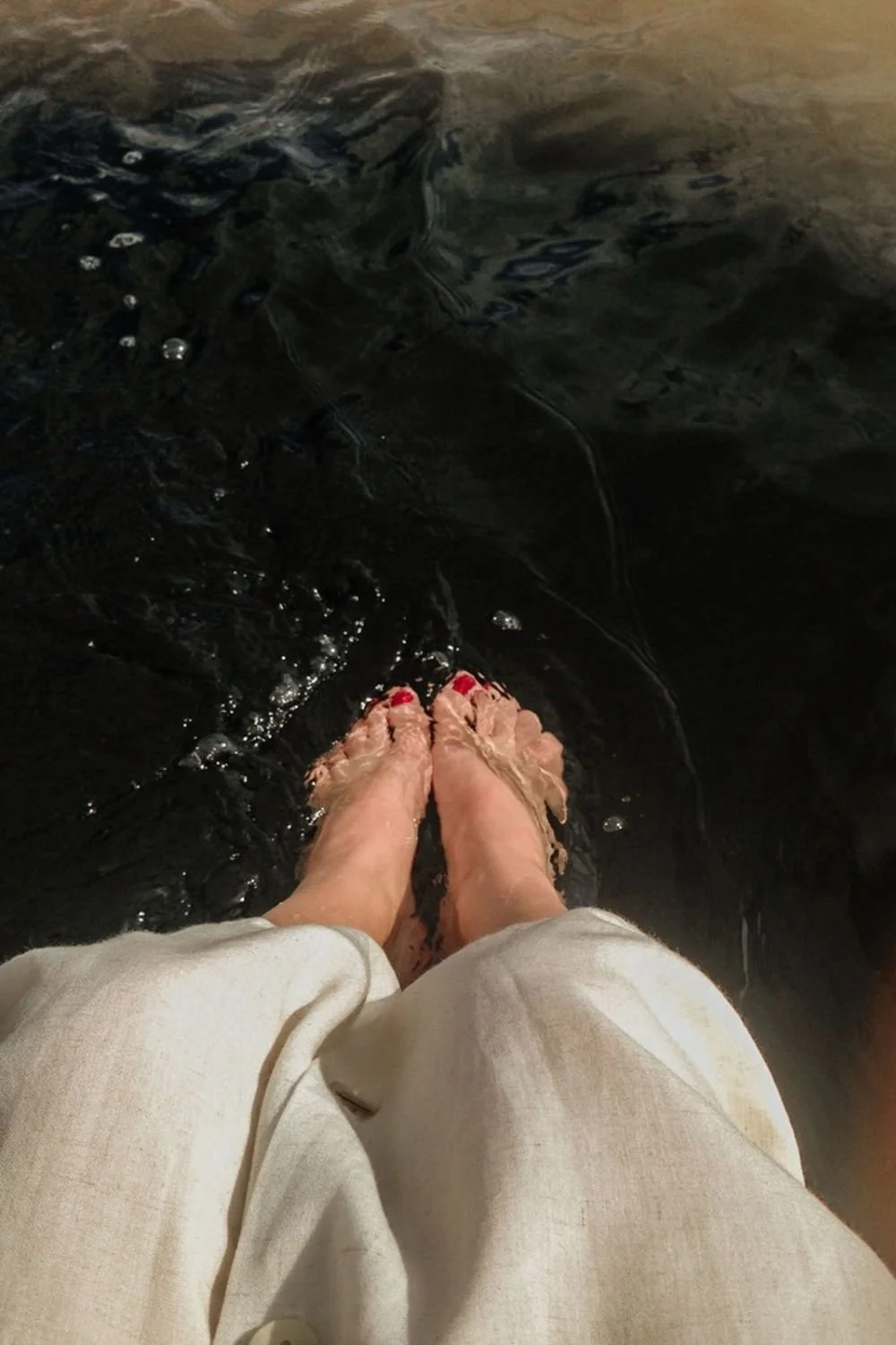 Woman in linen dress with red painted toes dipped in the water.