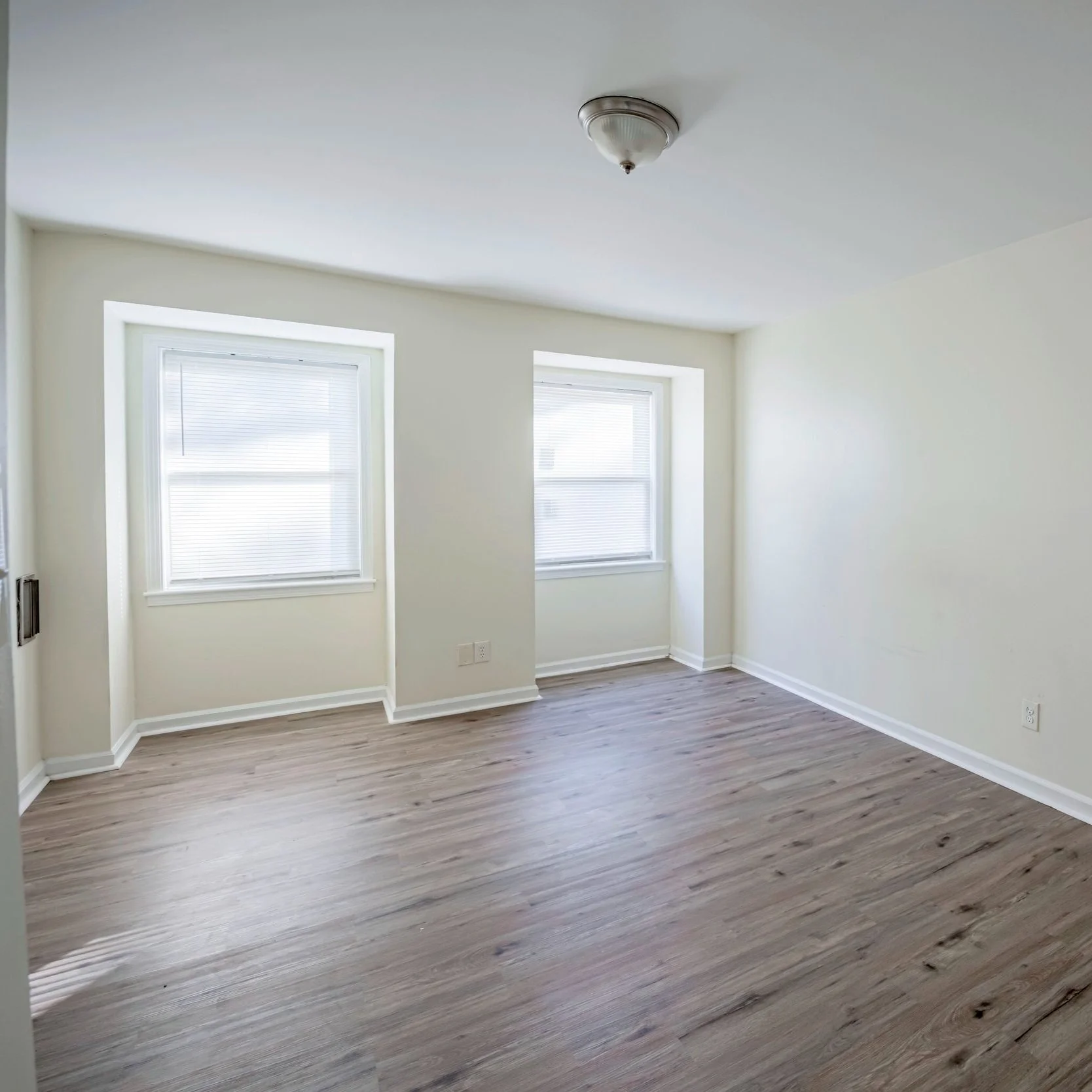 Empty room with two windows and light-colored hardwood floors.