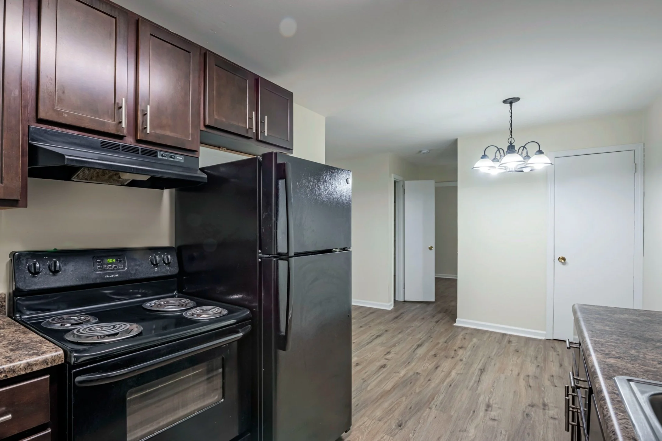 Kitchen with black stove, black refrigerator, dark brown cabinets, marble countertop, and a white ceiling with a chandelier light fixture.
