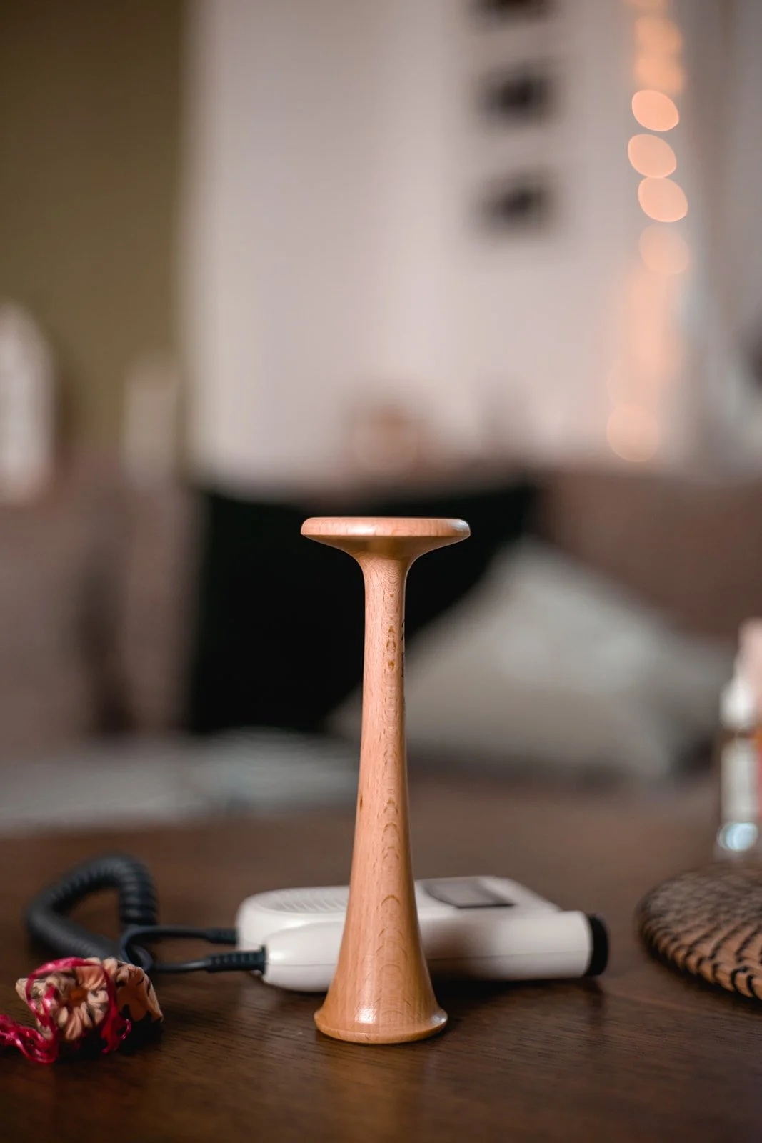 Ein Holzobjekt, das an einen Fuß oder eine Kerze erinnert, steht auf einem Tisch. Im Hintergrund sind ein Haartrockner, ein Hörer und andere Gegenstände sichtbar.