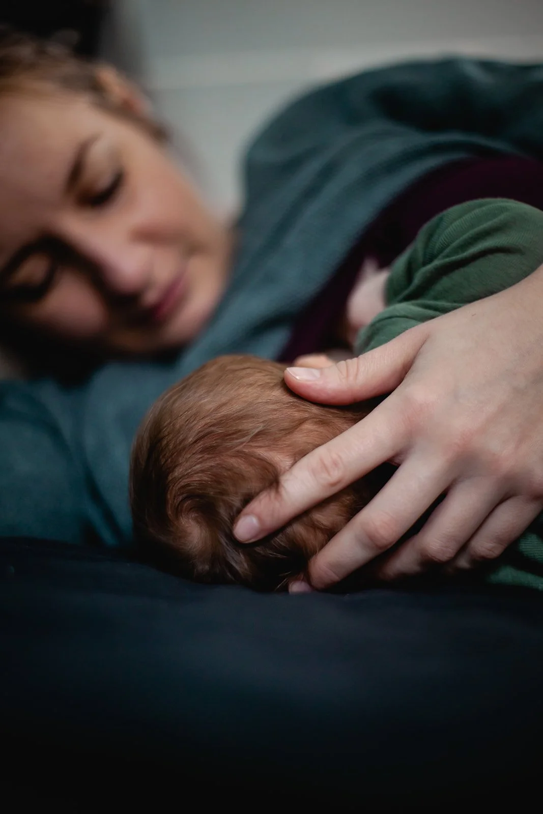 Eine Frau liegt auf der Seite und hält ein schlafendes Baby im Arm, beide erscheinen entspannt und geborgen.