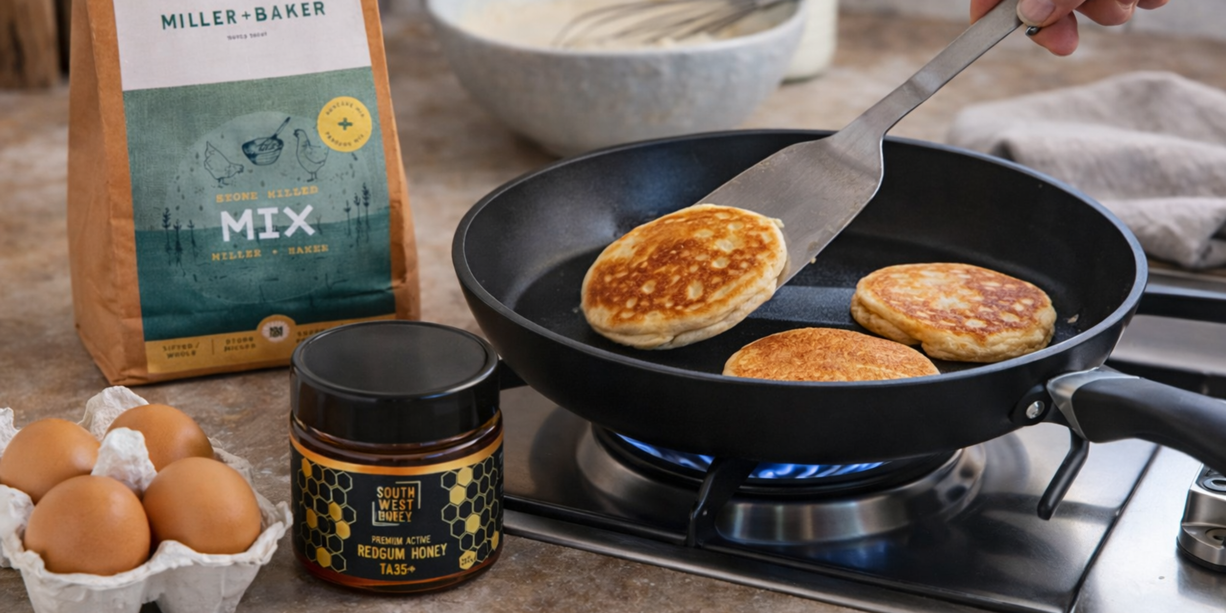 Western Australian pancake mix and South West Honey raw Western Australian Redgum honey jar next to a frying pan cooking fluffy pancakes