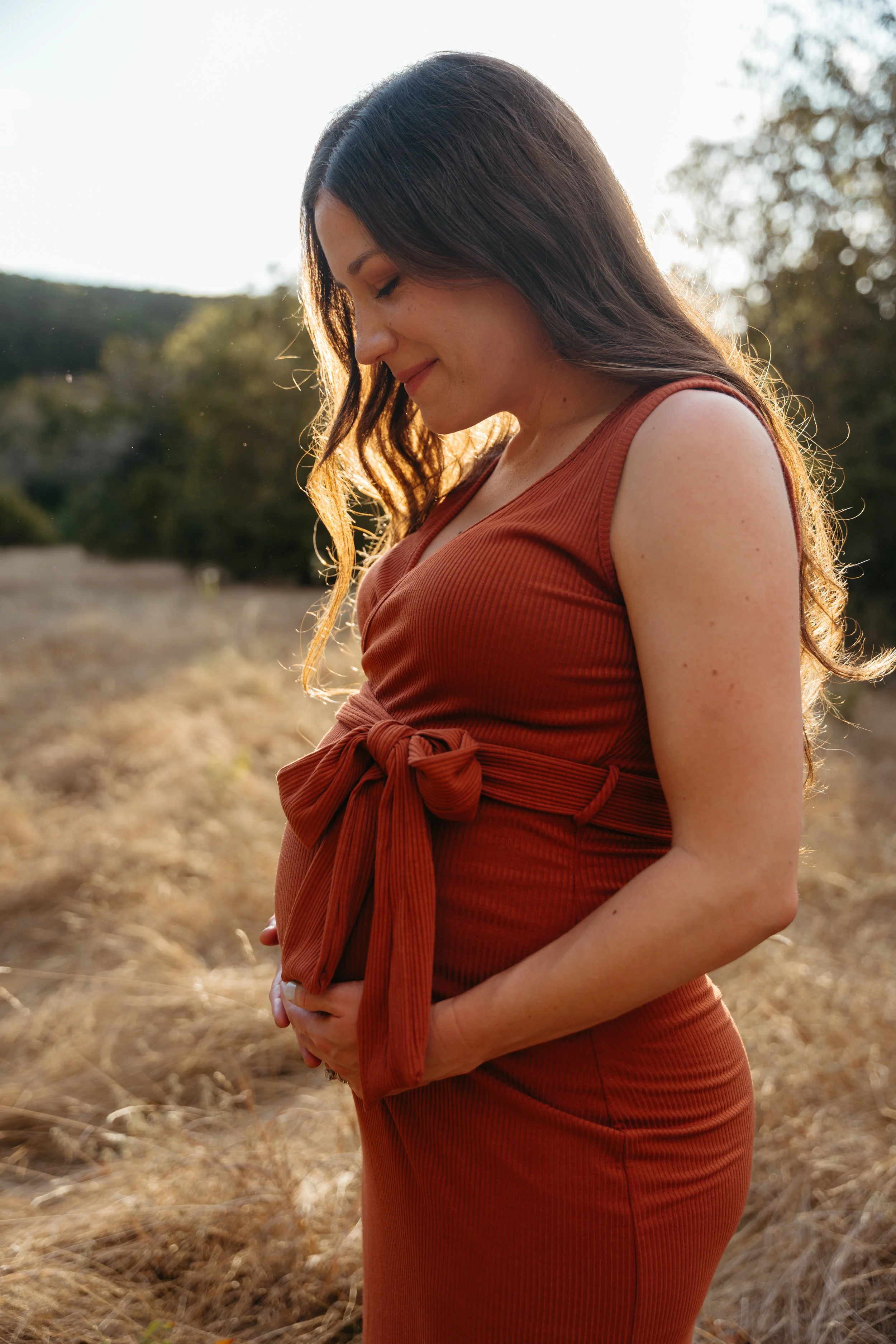 Pregnant woman gazes at her belly during a golden hour maternity photoshoot in Austin Texas.