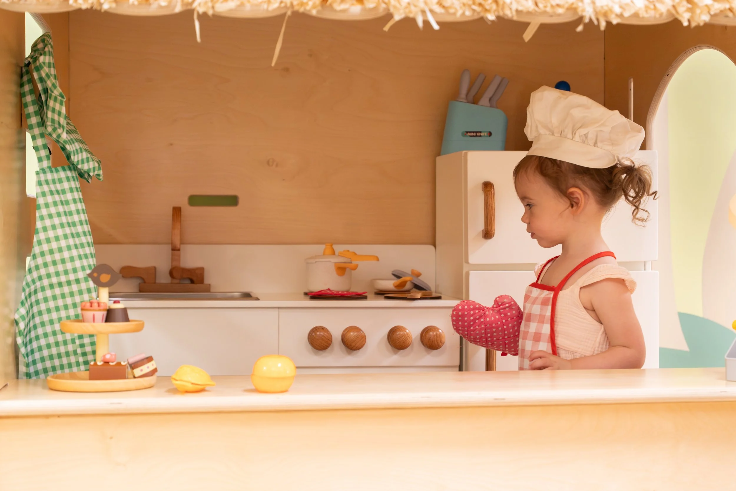 Child wears a chefs hat, oven mitt, and apron while playing in a playscape during an Austin brand Photography event.