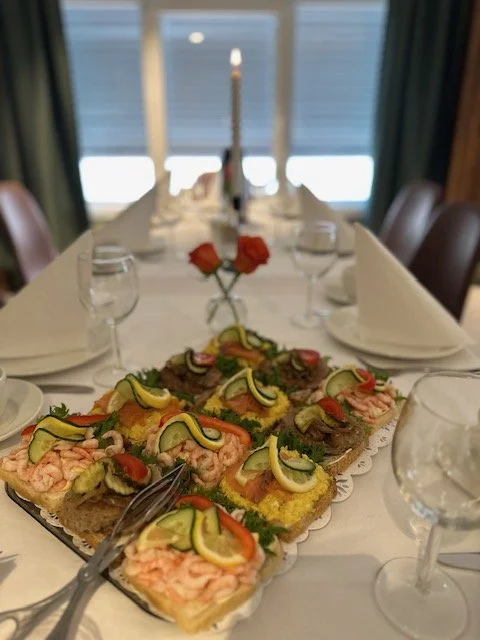 Festbord med smørbrød med reker, sitron, paprika, agurk og dill, dessert, vin og lysestake.