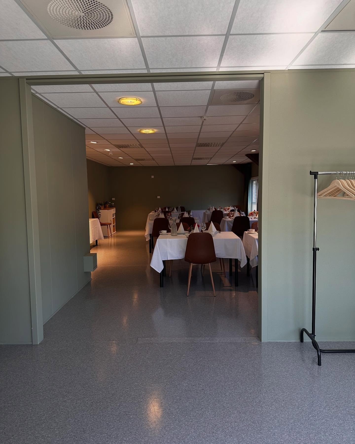 Et festlokale med runde bord dekket med hvite duker og stoler rundt, klar for besøk.