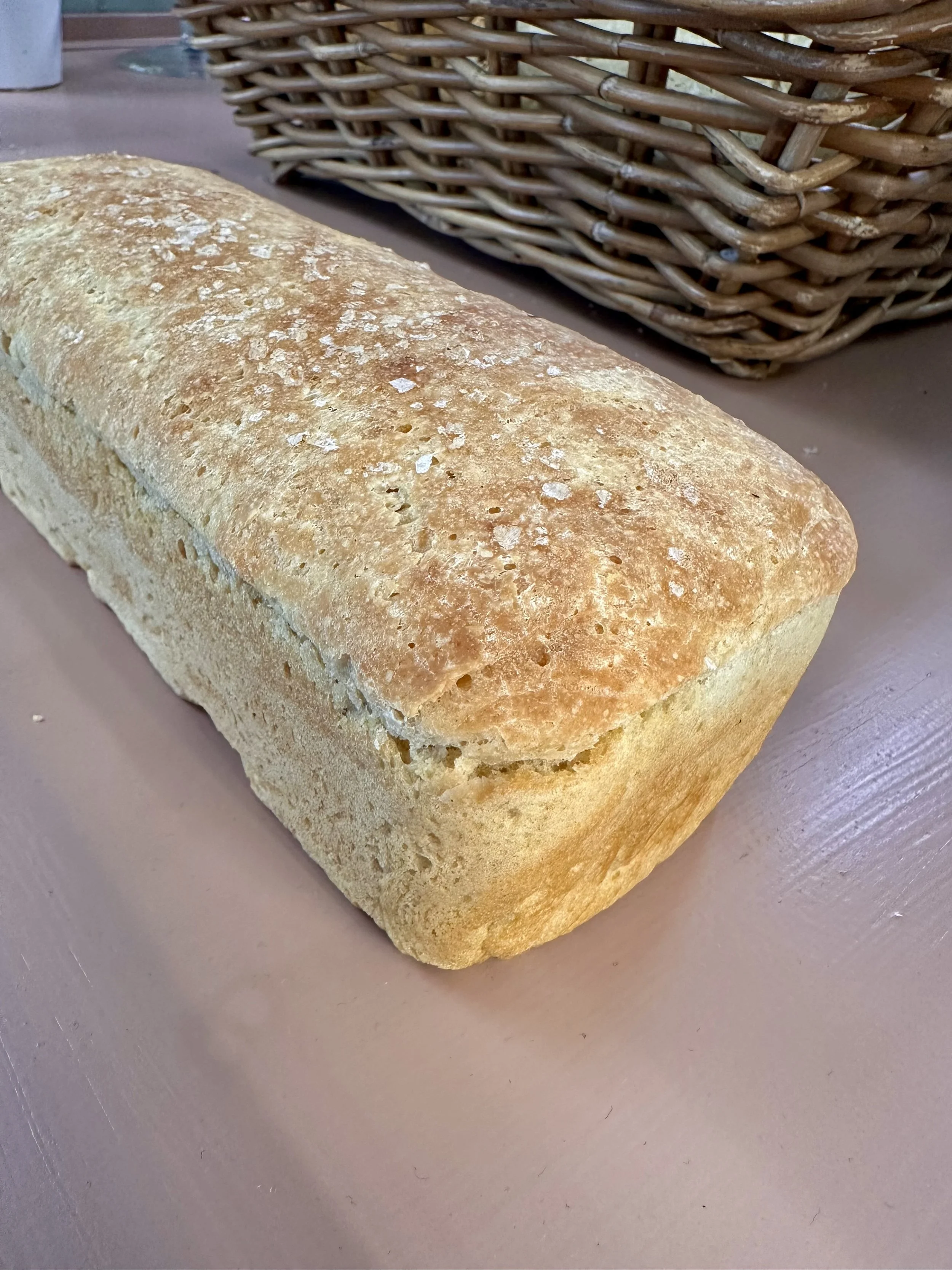 En rektangulær, gyldenfarget loff på en rosa overflate, med en veskekurv i bakgrunnen.