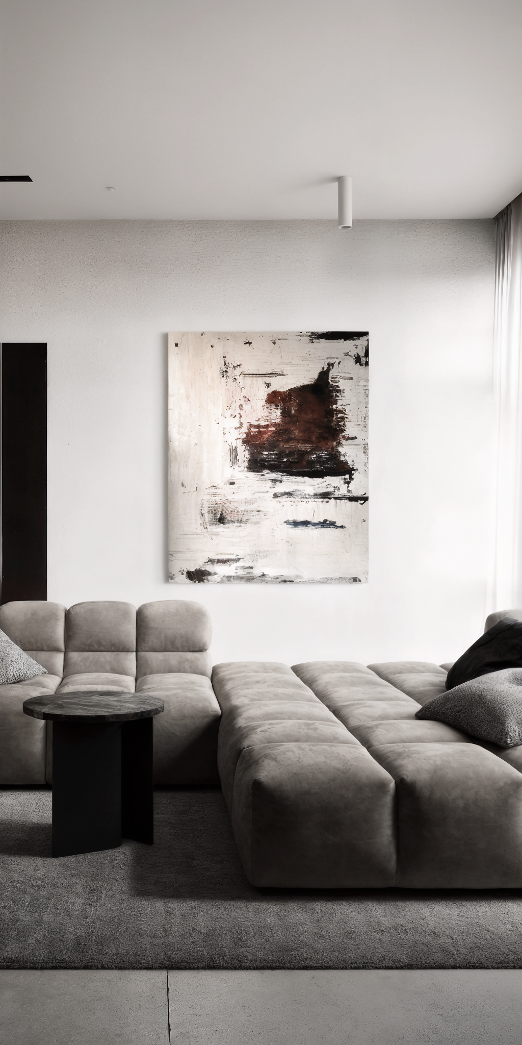 Modern living room with beige sectional sofa, abstract painting on white wall, small black side table, and gray rug.